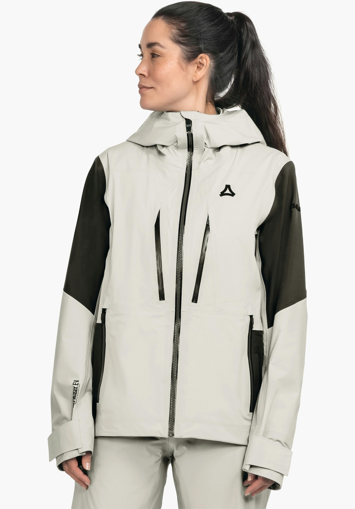 Shell Jk Style Lufeld WMS veste blanche avec manches vert foncé et logo Schöffel sur la poitrine; portée par une femme avec queue de cheval regardant de côté; fond studio blanc. Aucun texte lisible.