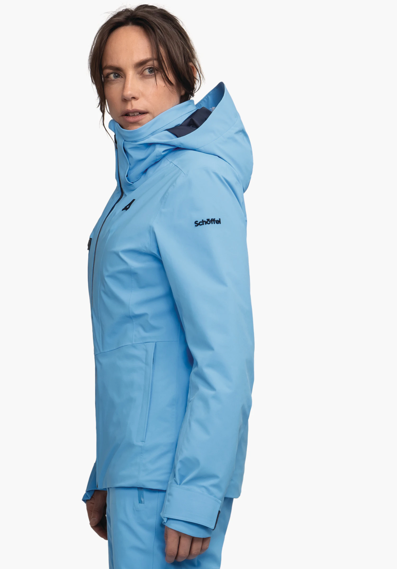 Jacket Style Pontre WMS veste blanc clair, portée par une femme; elle sourit et regarde vers le haut, debout de profil devant fond clair neutre. Impression sur la manche: "Schöffel". Cheveux brun foncé, queue de cheval.