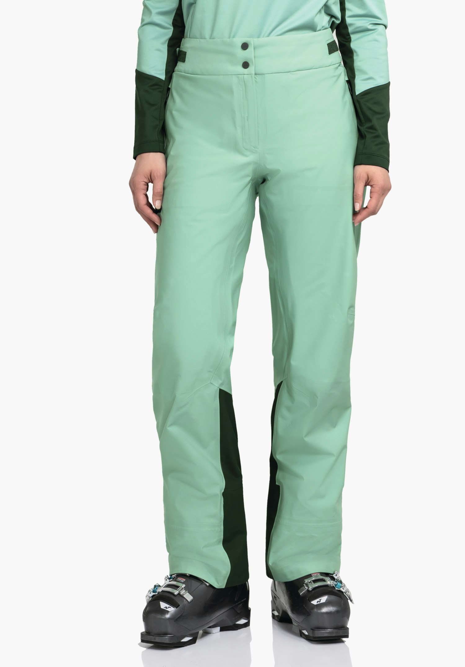 Pants Style Lufeld WMS hellgrüne Hose, getragen von stehender Person; Hände seitlich, dunkelgrüne Einsätze an Taille und Innenbeinen, schwarze Skischuhe, weißer Hintergrund.