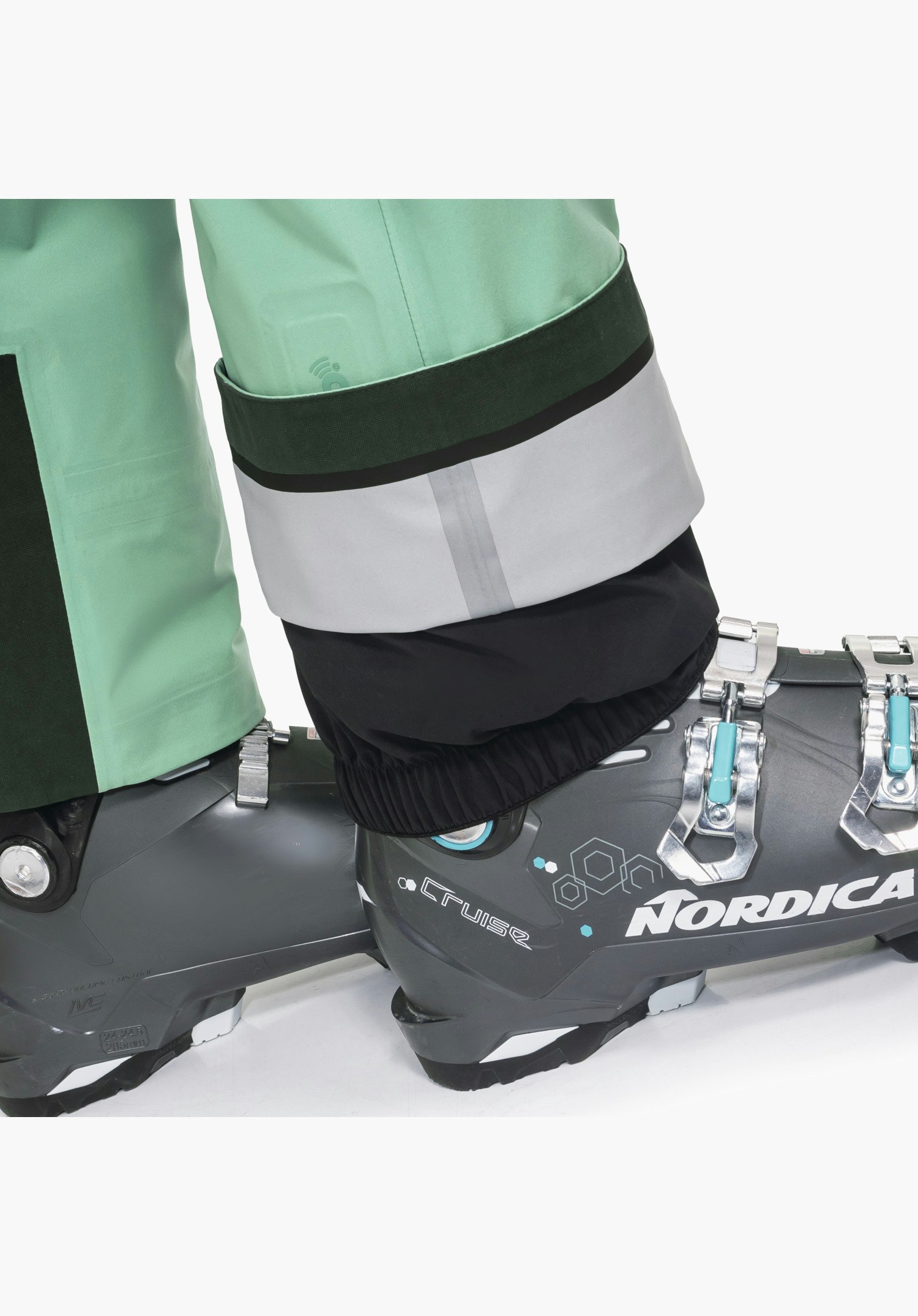 Pants Style Lufeld WMS Detailansicht des grünen Beinabschlusses mit verstärktem Kantenschutz, RECCO®-Reflektor und fixiertem Schneefang am Skischuh, Nahaufnahme vor weißem/neutralem Hintergrund.