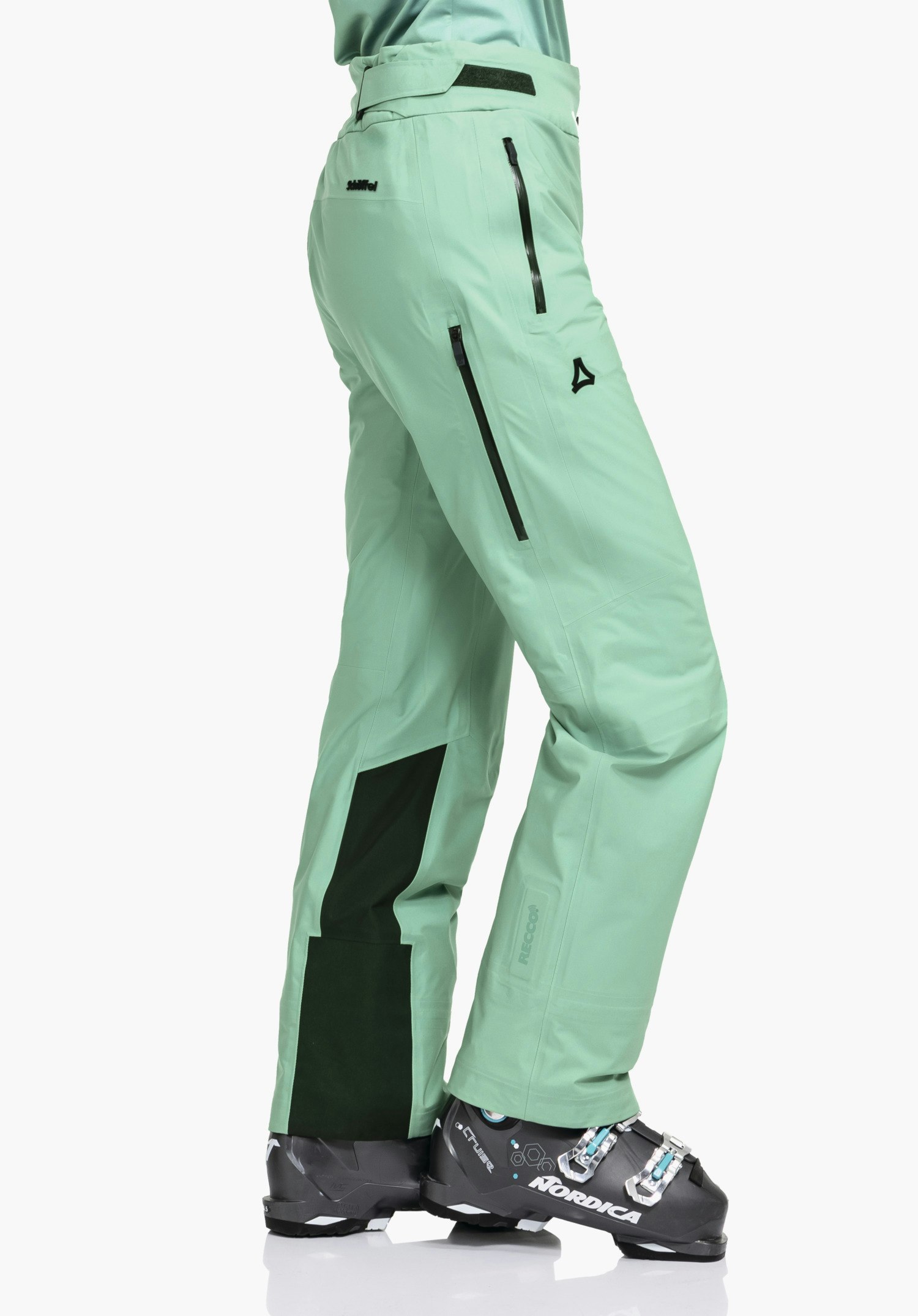 Pants Style Lufeld WMS hellgrüne Skihose, getragen von stehender Person im Profil, mit schwarzen Reißverschlüssen und dunkelgrüner Unterschenkel-Verstärkung, Schöffel-Logo auf Oberschenkel; Text: "Schöffel", "RECCO", "NORDICA".