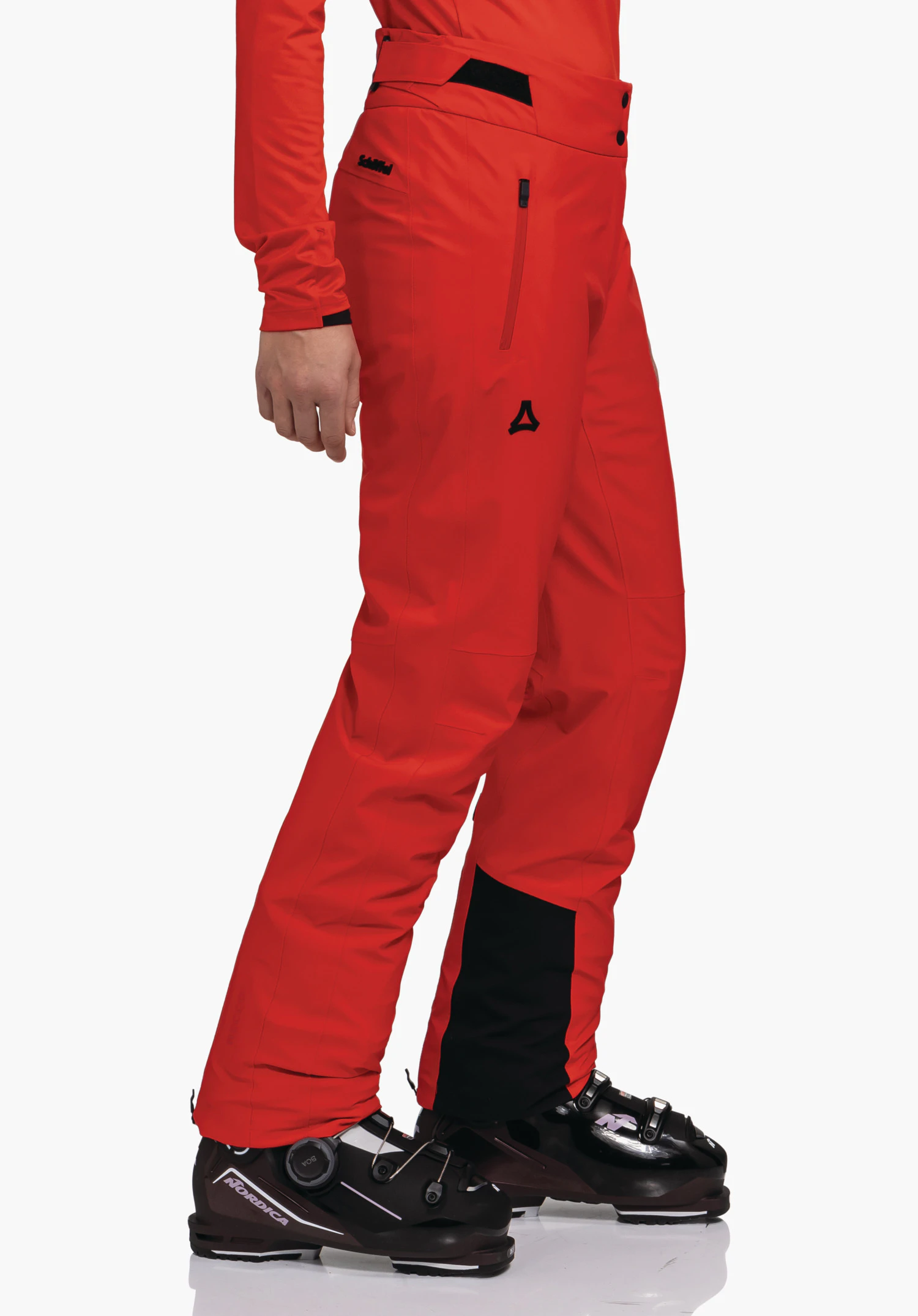 Pants Style Skayra WMS rode skibroek, zijwaarts gedragen; persoon staat op zwarte skischoenen voor een witte achtergrond; zwart Schöffel-logo op het bovenbeen, tekst "Schöffel" op de heup; "Nordica" op de schoen.
