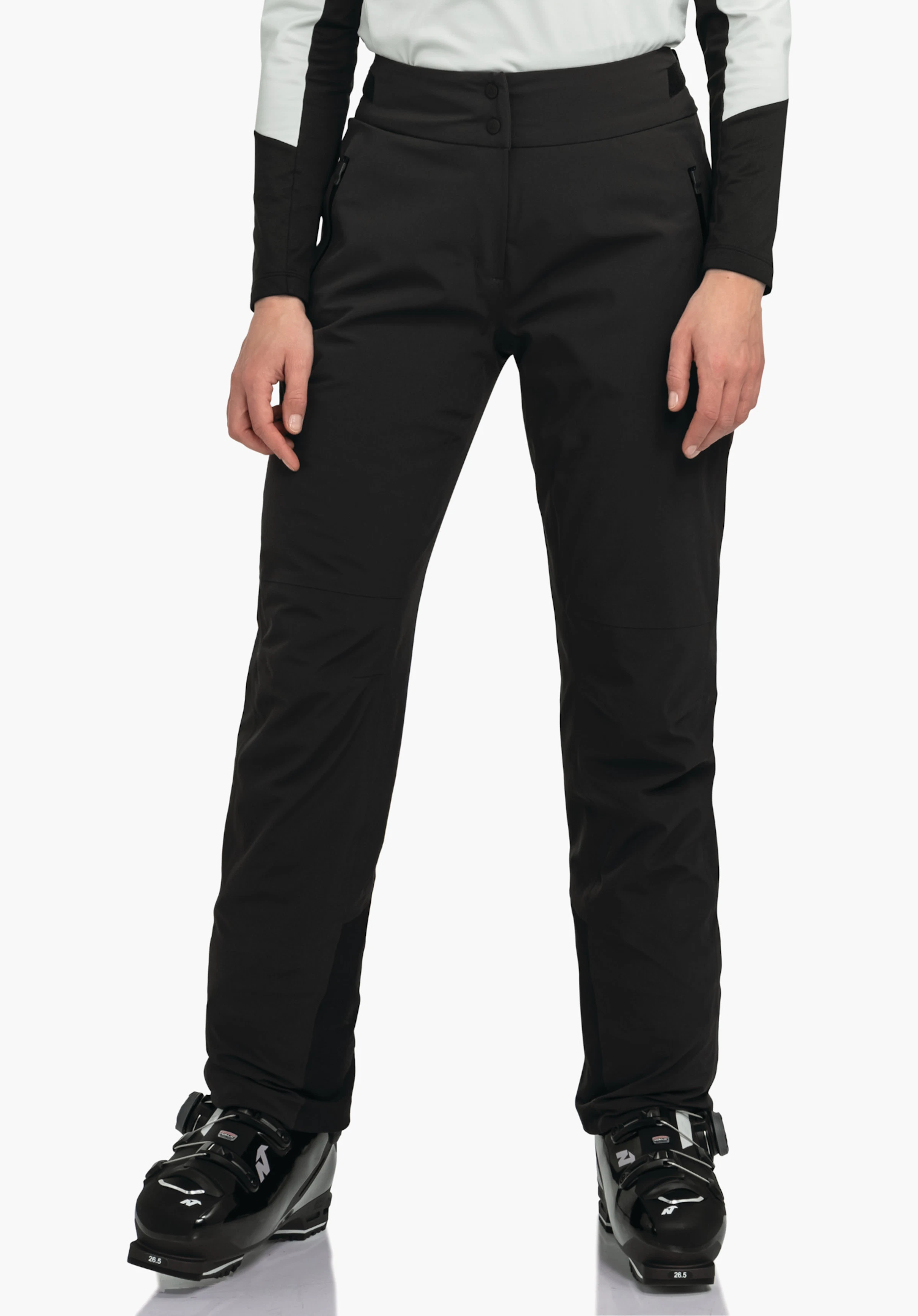 Pants Style Skayra WMS Schwarze Skihose; Person steht gerade mit Händen seitlich, trägt weißes Oberteilärmel und schwarze Skischuhe. Studio-Umgebung, weißer Hintergrund. Text auf Schuh: 26.5.