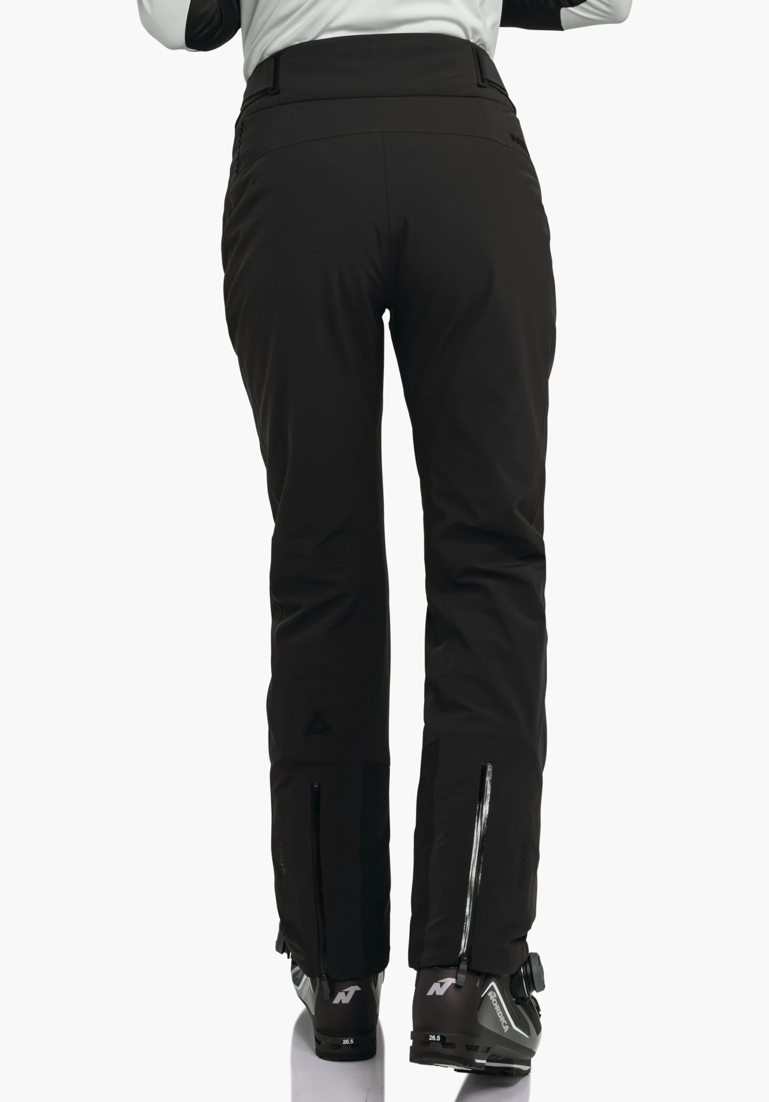 Pants Style Skayra WMS zwarte skihose, gedragen door een persoon in achteraanzicht voor een witte achtergrond; skischoenen met opschrift "N" en "26.5" zichtbaar, Schöffel-logo op het onderbeen.