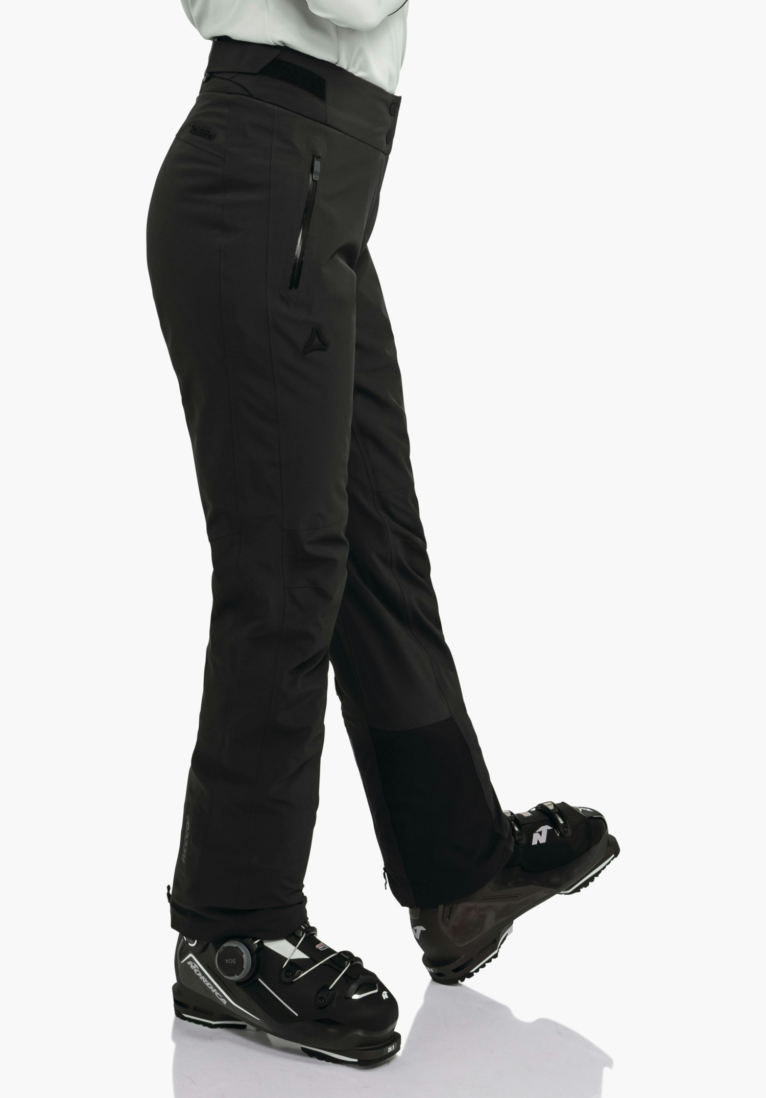 Pants Style Skayra WMS diepzwarte skibroek met Schöffel-logo, bedekt de benen; persoon staat met gekruiste benen en draagt diepzwarte skischoenen; witte achtergrond. Tekst: "Schöffel".