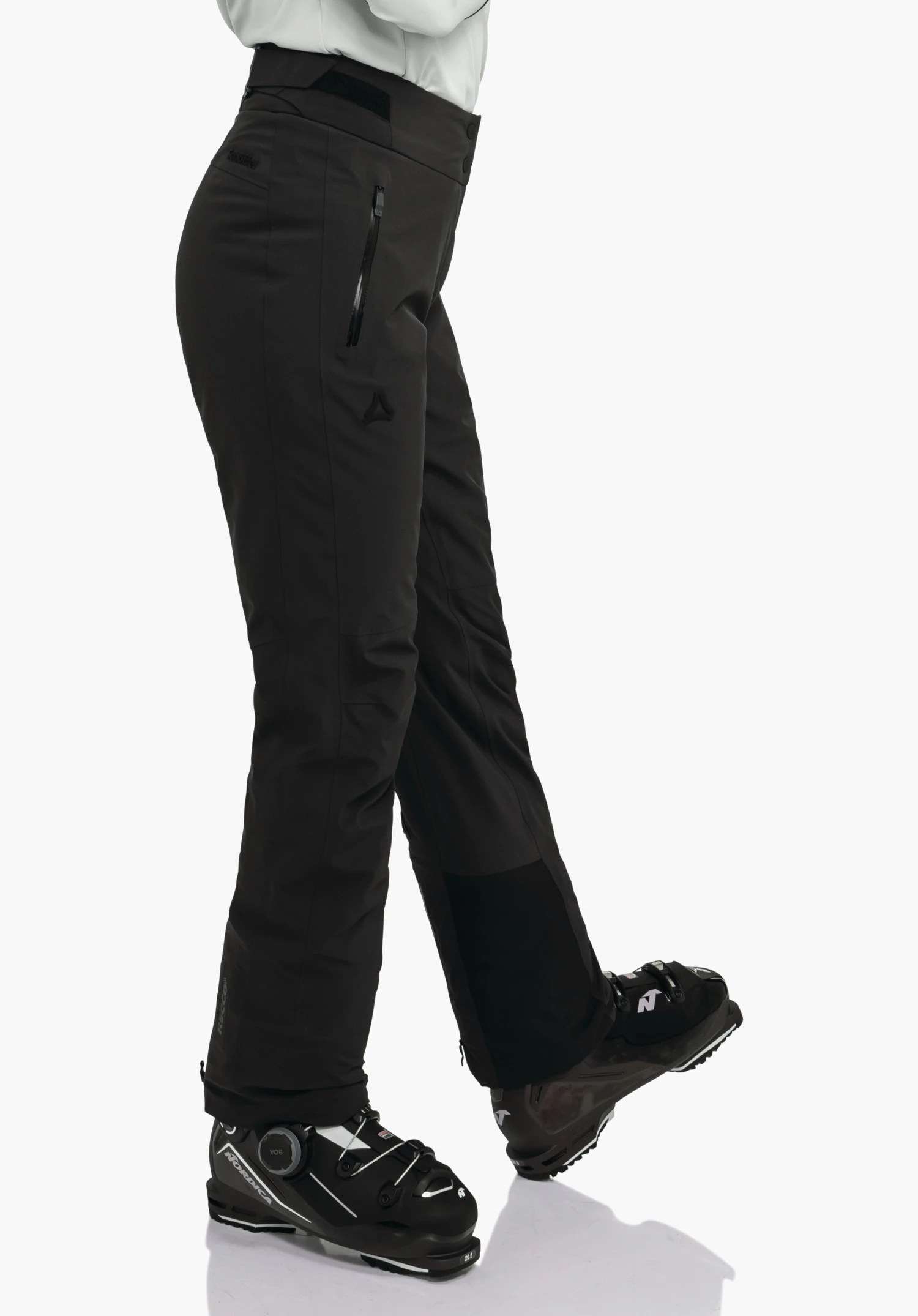 Pants Style Skayra WMS diepzwarte skibroek met Schöffel-logo, bedekt de benen; persoon staat met gekruiste benen en draagt diepzwarte skischoenen; witte achtergrond. Tekst: "Schöffel".