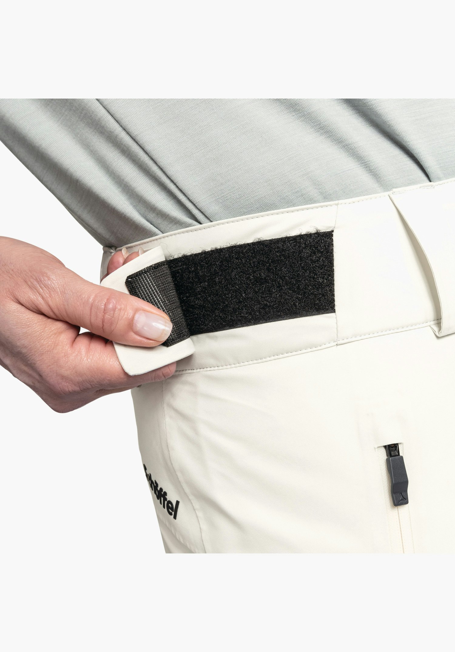 Pants Style Pine WMS détail de la ceinture réglable de couleur nature. Une fermeture velcro noire pour l'ajustement de la largeur est présentée, avec une fermeture éclair et l'inscription Schöffel partiellement visible en dessous. Gros plan sur fond blanc/neutre.