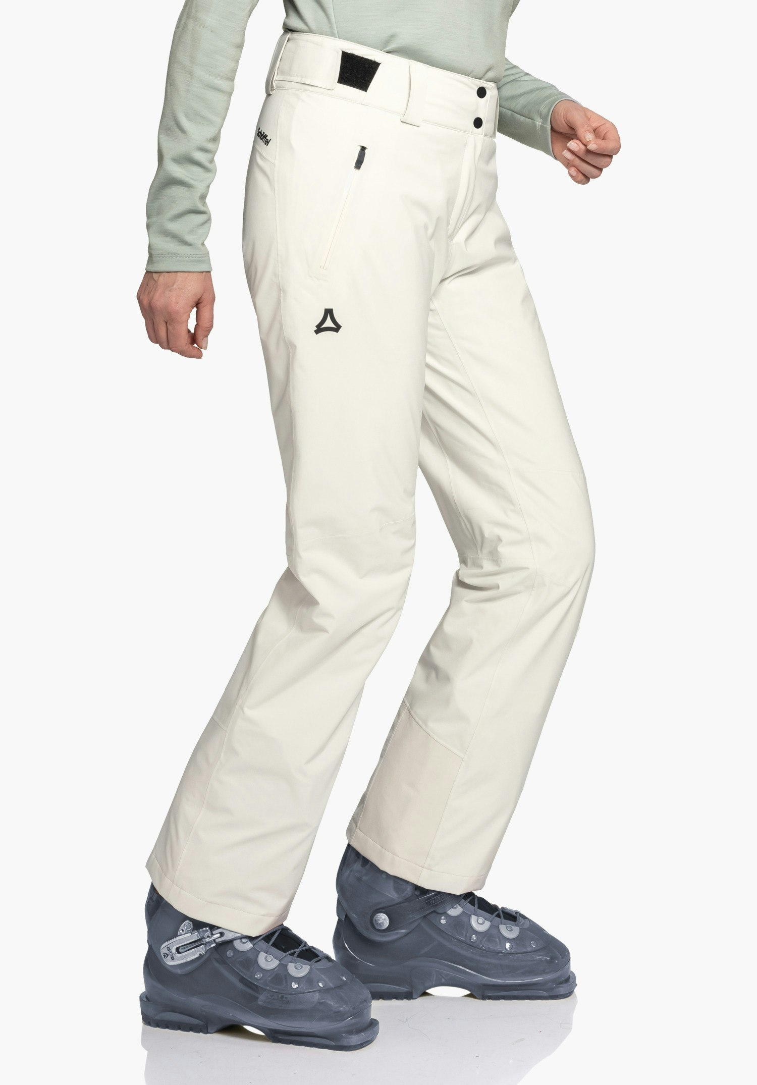 Pants Style Pine WMS pantalon de ski blanc clair, porté avec un pas légèrement vers l’avant; la personne porte des chaussures de ski bleu foncé, haut vert clair visible. Inscription à la taille: «schöffel», logo Schöffel noir supplémentaire.