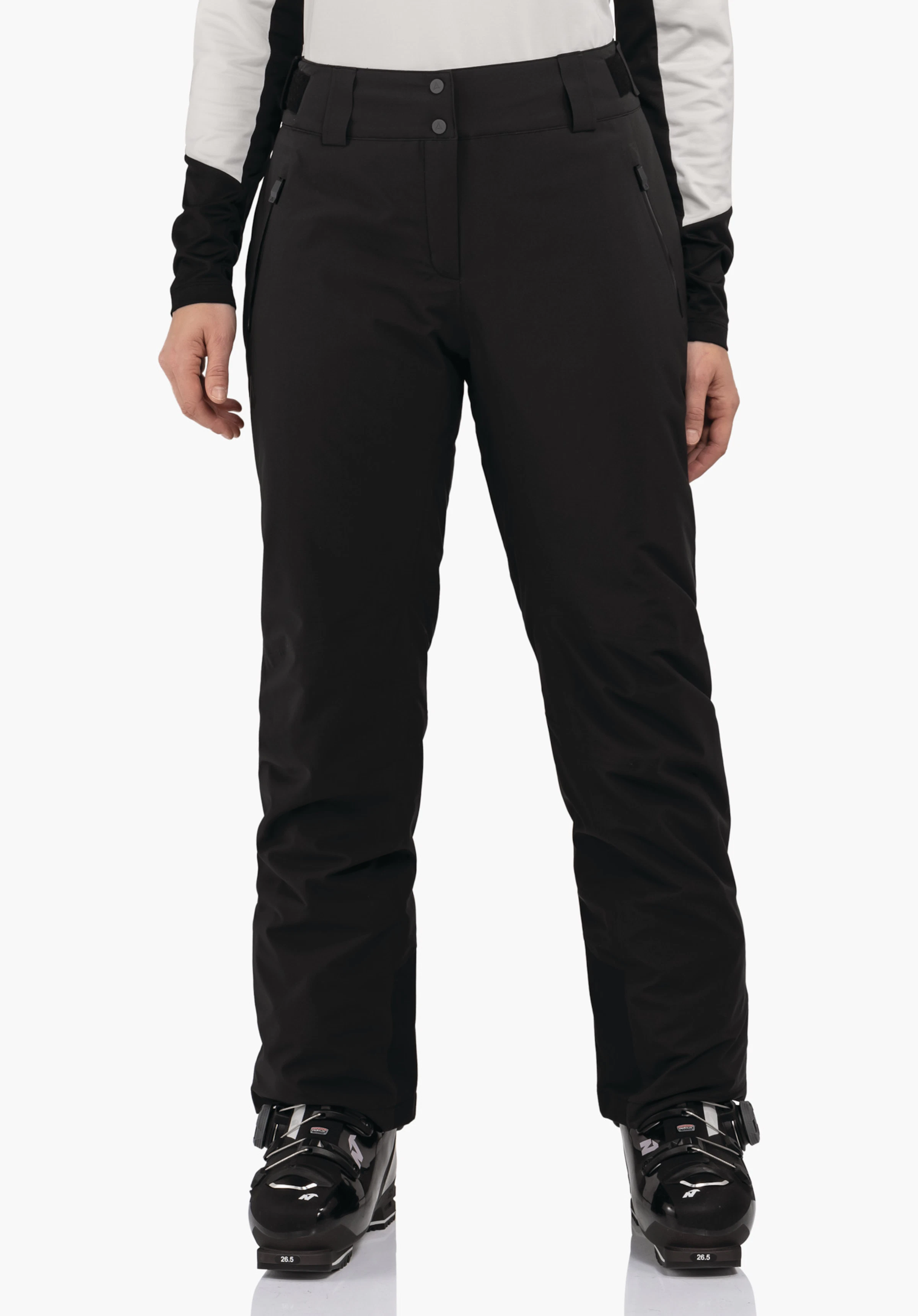 Pants Style Pine WMS Schwarze Skihose, getragen von stehendem Modell, frontal fotografiert; weiße Ärmel sichtbar, schwarze Skischuhe mit Text "26.5"; weißer Hintergrund.