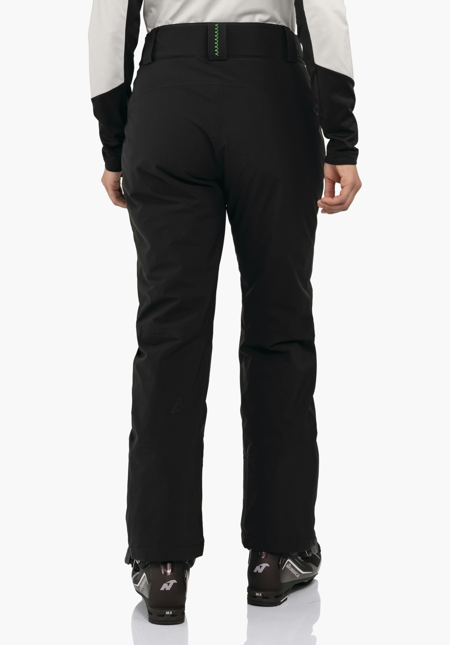 Pants Style Pine WMS pantalon de ski noir — porté de dos, debout sur des chaussures de ski devant un fond blanc; logo Schöffel sur le bas de la jambe. Textes visibles: Nordica, 26.5, N.