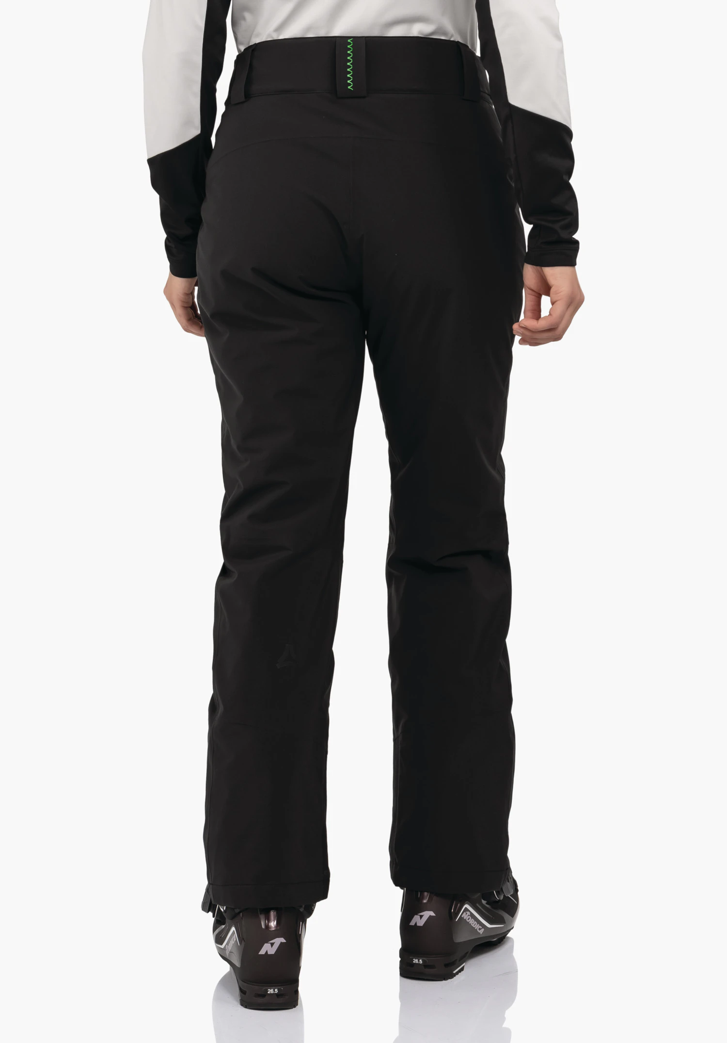 Pants Style Pine WMS zwarte skihose, van achteren gedragen; persoon staat op skischoenen voor een witte achtergrond, Schöffel-logo op het onderbeen. Zichtbare tekst: Nordica, 26.5, N.