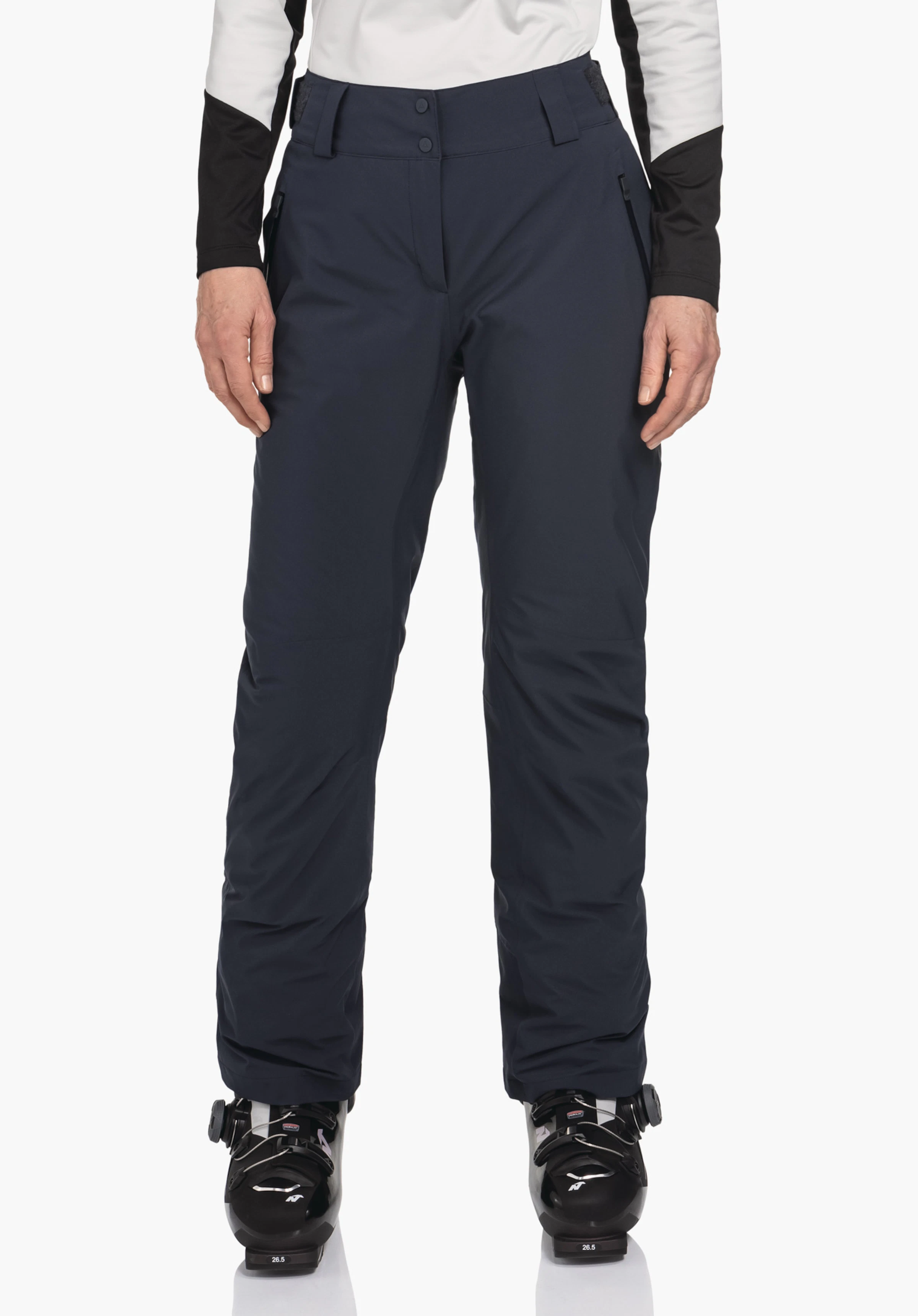 Pants Style Pine WMS Dunkelblaue Skihose, getragen von stehender Person; Hände hängen seitlich, weißes Oberteil mit schwarzen Einsätzen, schwarze Skischuhe, neutraler weißer Hintergrund.