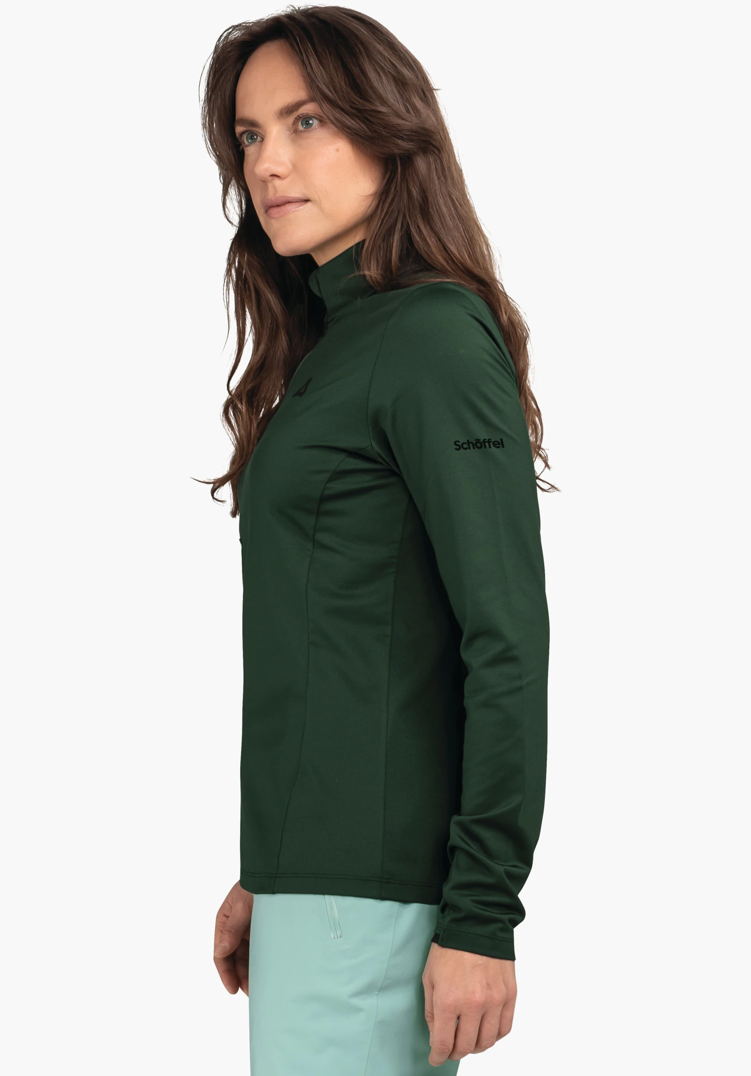 Longsleeve Style Pine WMS dark green, fitted long-sleeve top with stand-up collar (Schöffel logo on chest), model stands side-on in front of a white background; light green trousers visible. Text: "Schöffel".