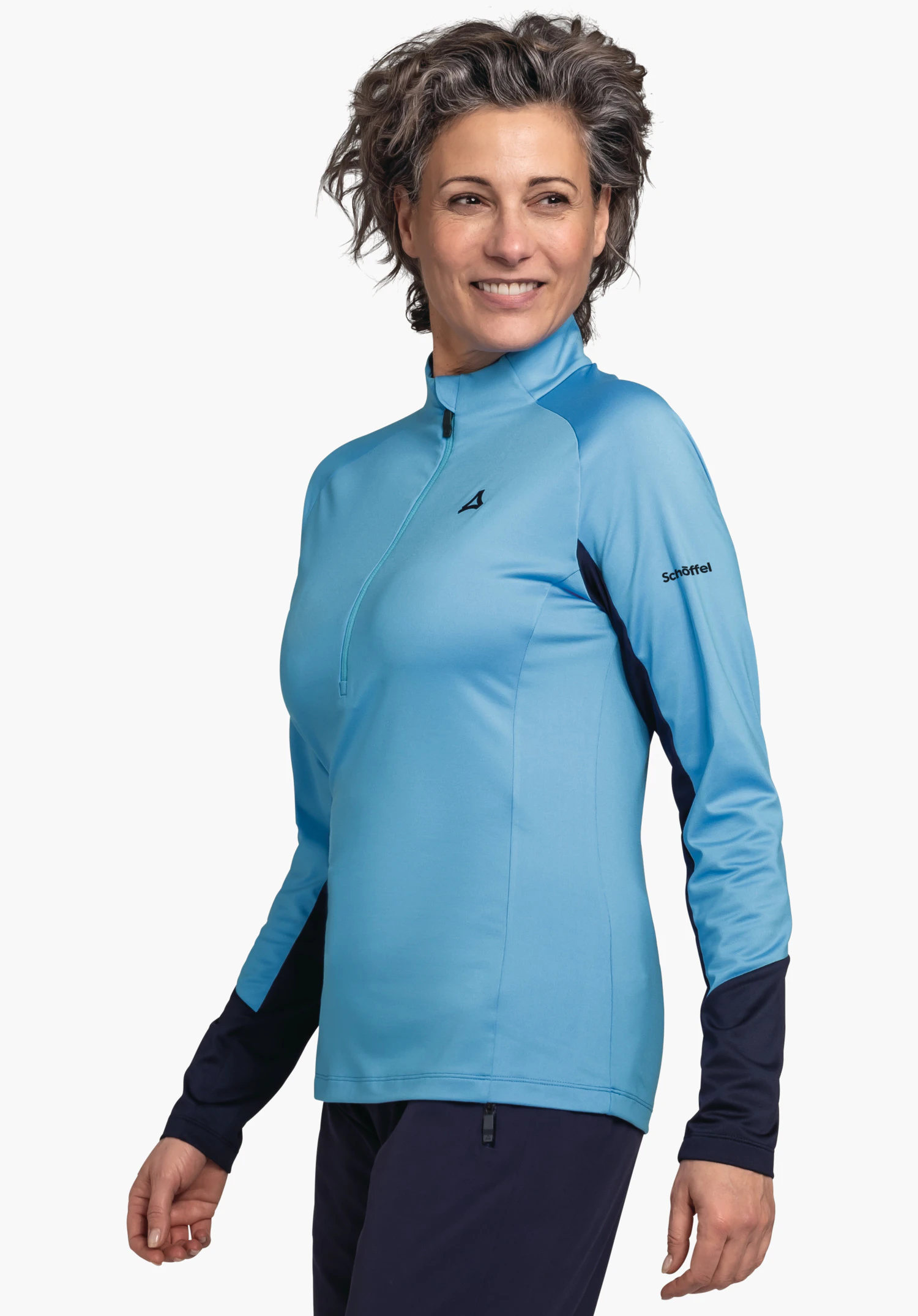 Longsleeve Style Safoon WMS lichtblauw longsleeve-shirt met Schöffel-logo op de borst en tekst "Schöffel" op de mouw; vrouw glimlacht en kijkt naar rechts; donkerblauwe mouw- en broekdelen; witte achtergrond.