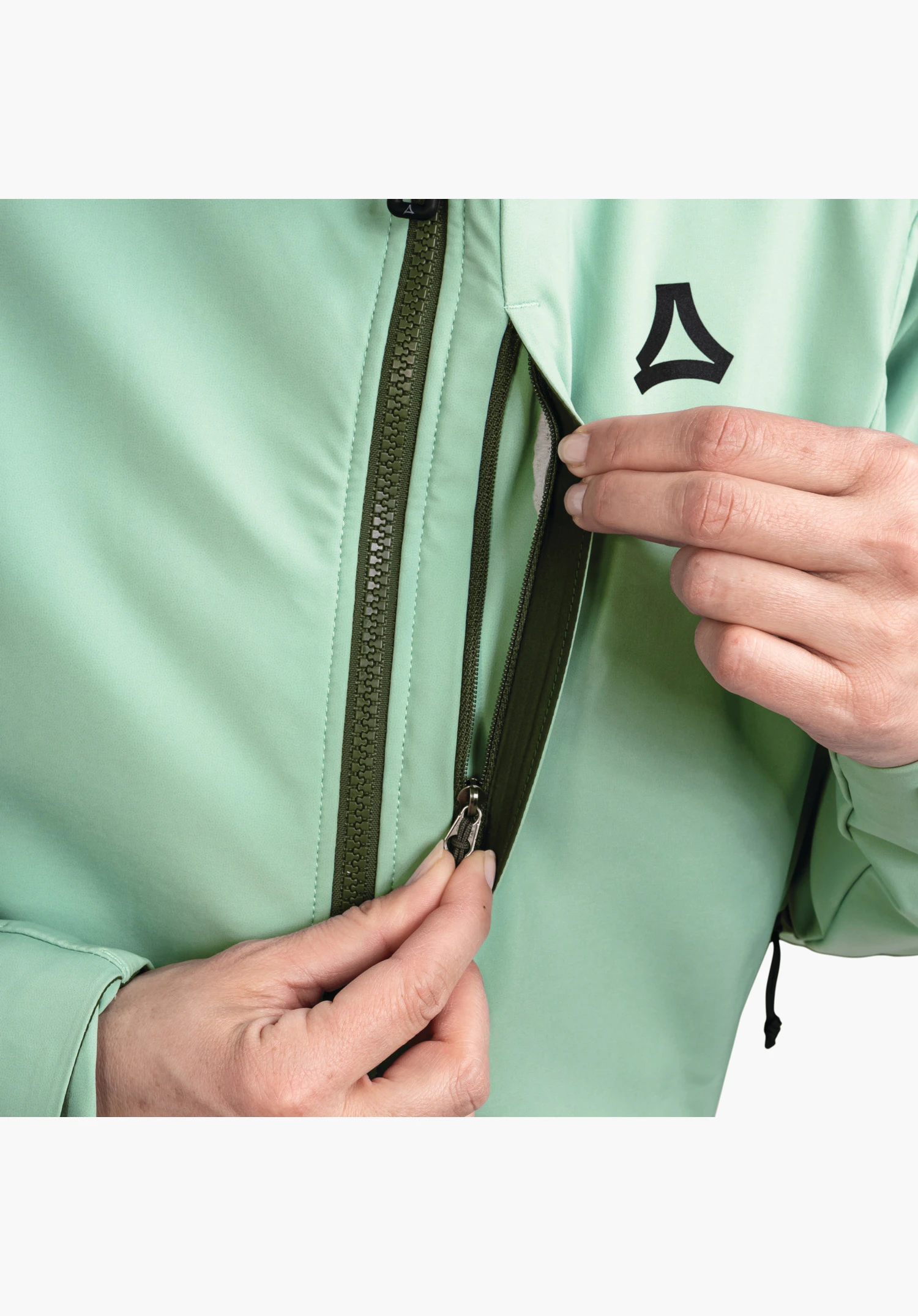 Softshell Jk Style Milagle WMS montre la poche poitrine zippée, la fermeture éclair frontale vert foncé et le logo Schöffel sur le tissu vert. Gros plan sur fond blanc.