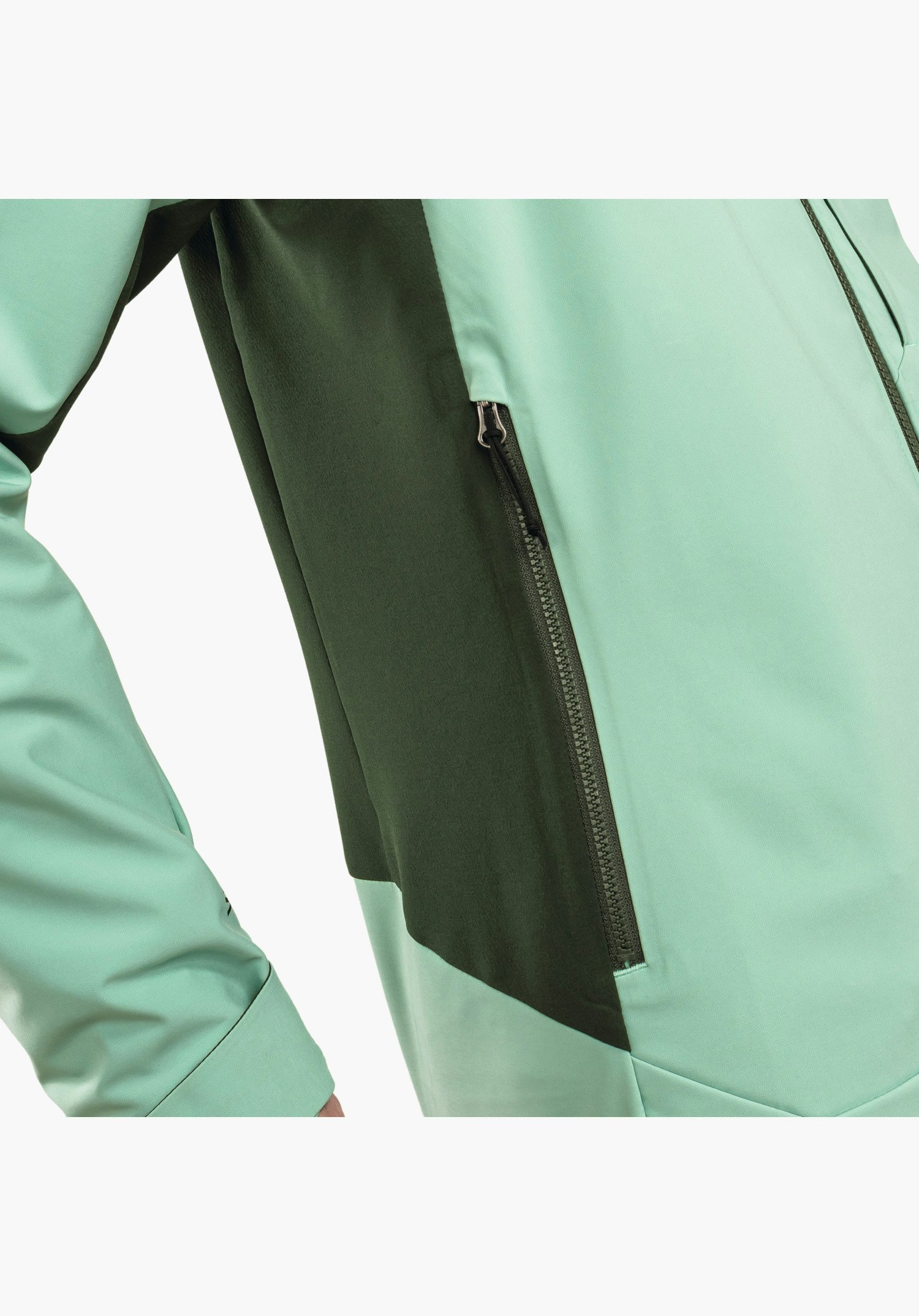 Softshell Jk Style Milagle WMS mit Fokus auf die seitliche Reißverschlusstasche, die in einen dunkelgrünen Farbeinsatz integriert ist und sich vom helleren Grünton des Softshell-Materials abhebt, Nahaufnahme vor weißem Hintergrund.