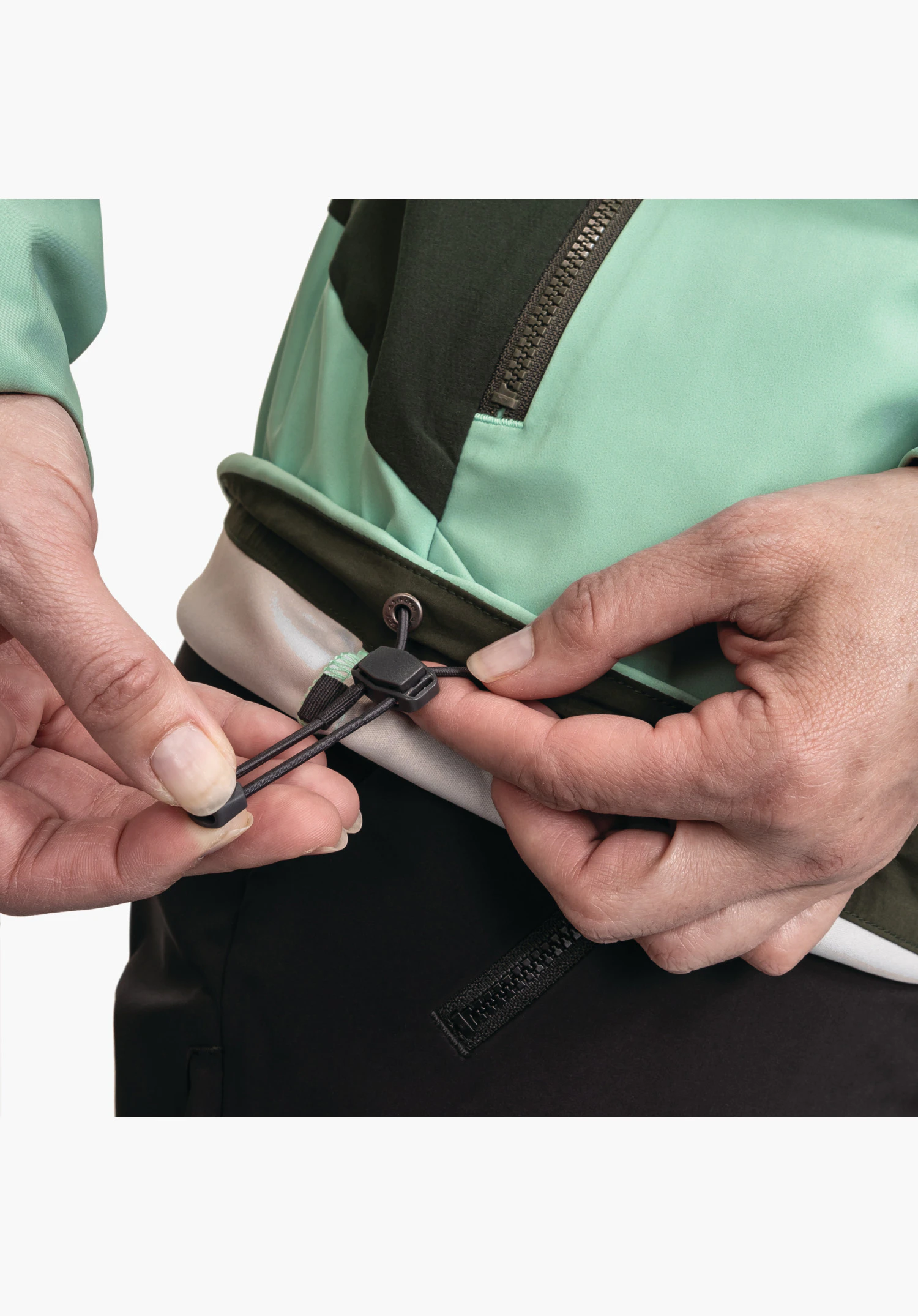 Softshell Jk Style Milagle WMS, vue détaillée des mains ajustant l'ourlet réglable avec un cordon élastique et un stoppeur sur la veste verte, gros plan sur fond blanc/neutre.