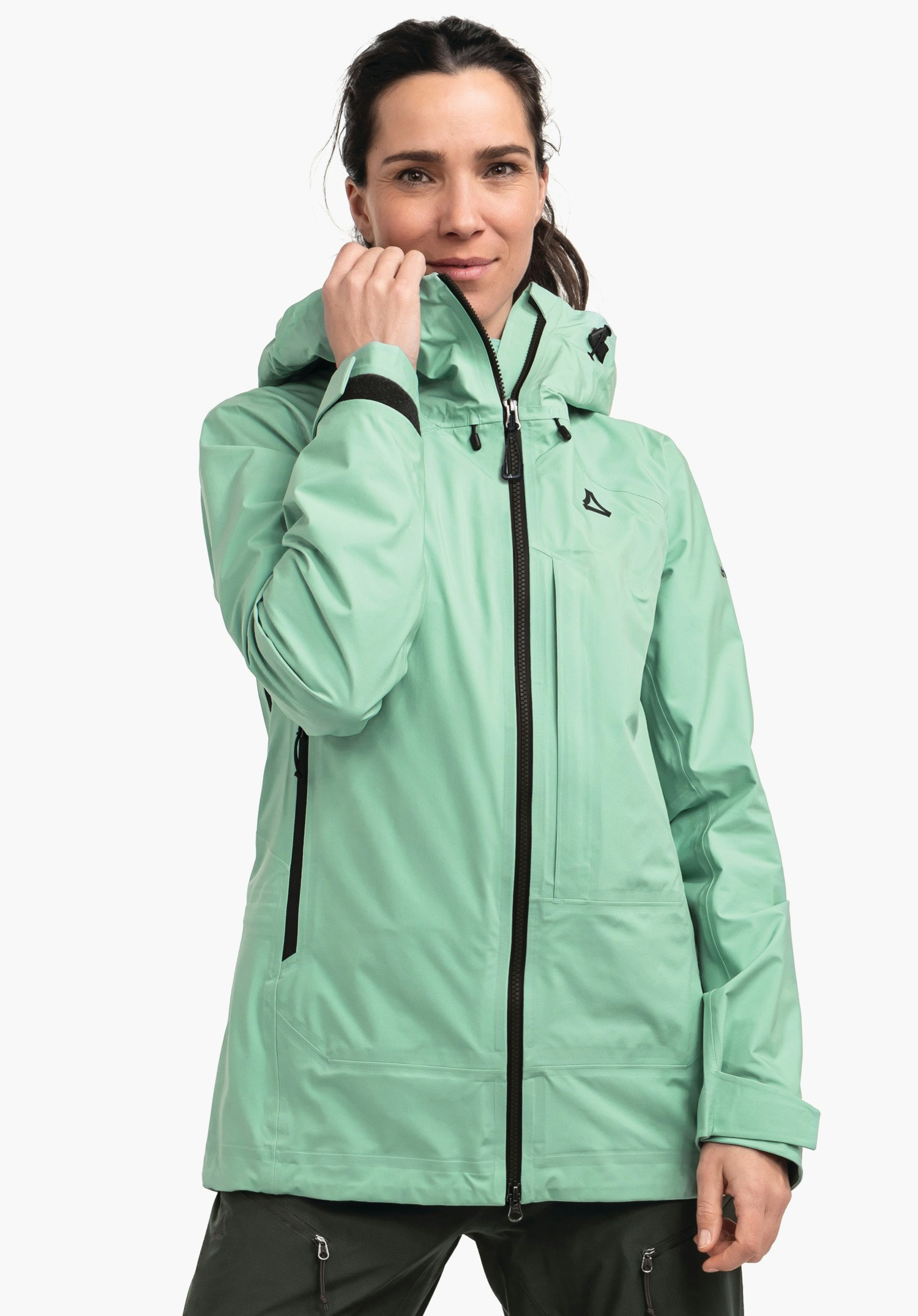Jacket Style Milagle WMS light green outdoor jacket; woman pulls the zip up at the collar, Schöffel logo on the chest, black zips and details, hood; standing shot against a white background.