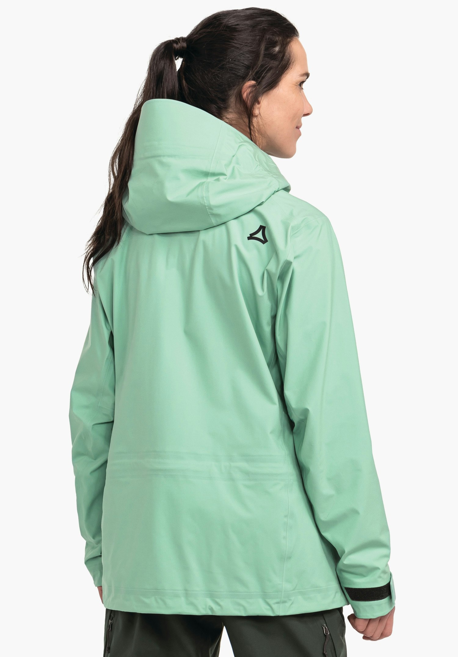 Jacket Style Milagle WMS light green rain jacket, rear view; woman wears it with hood up and looks right; Schöffel logo on the right shoulder; light neutral background.