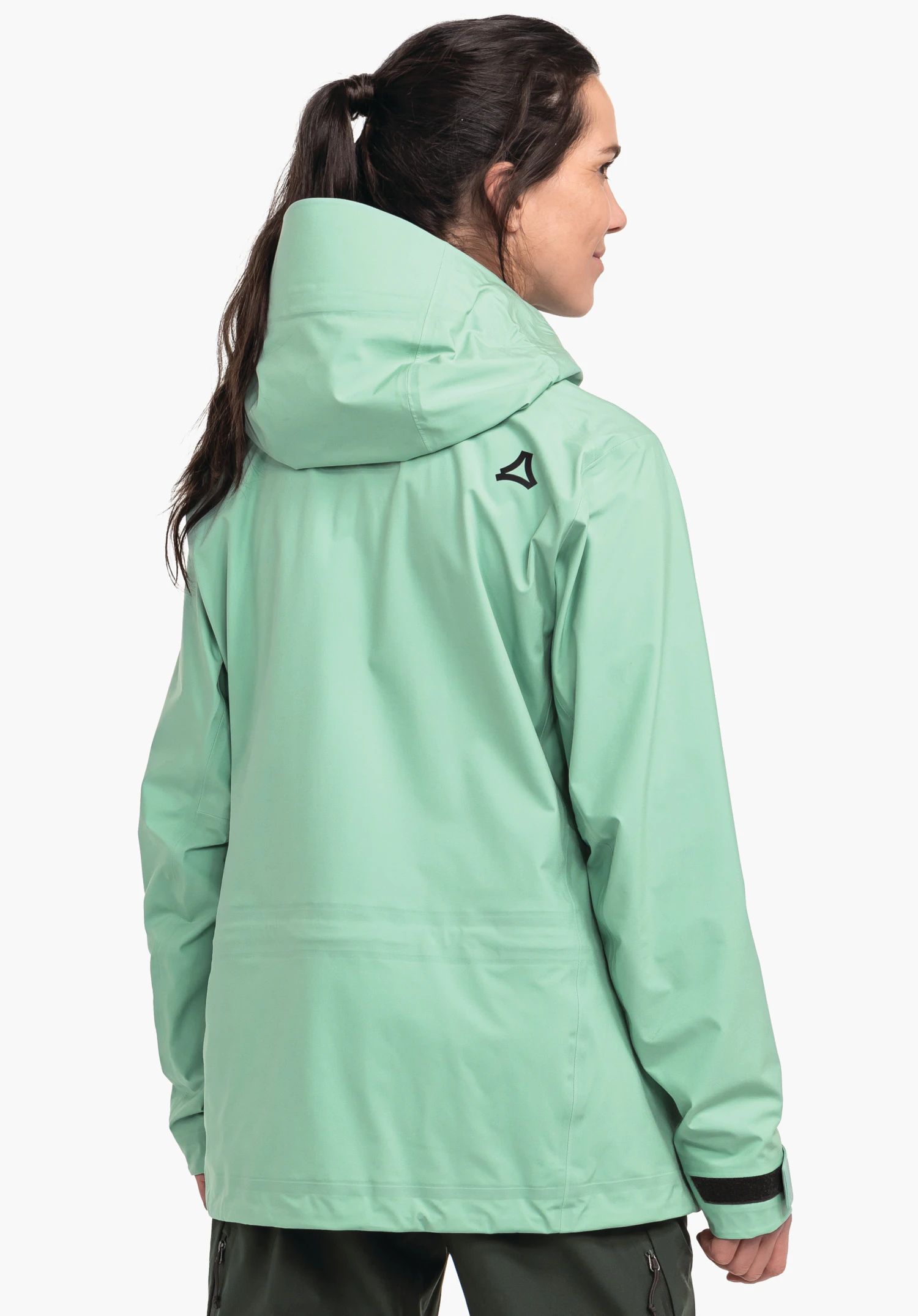 Jacket Style Milagle WMS veste imperméable vert clair, vue arrière; femme portant la capuche relevée et regardant vers la droite; logo Schöffel sur l’épaule droite; fond clair neutre.