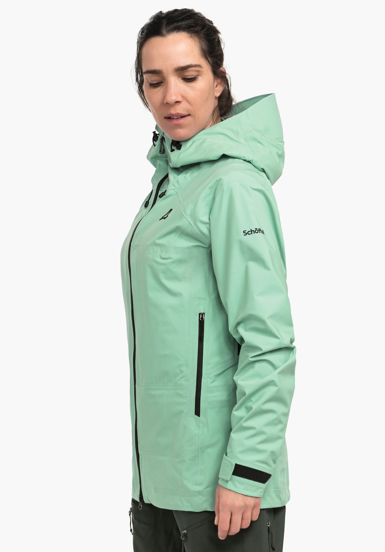 Jacket Style Milagle WMS jacket; person wears a light green hip-length rain jacket with hood and black zips, looks side-on and downwards in front of a white background. Text: "Schöffel". Triangular Schöffel logo visible.