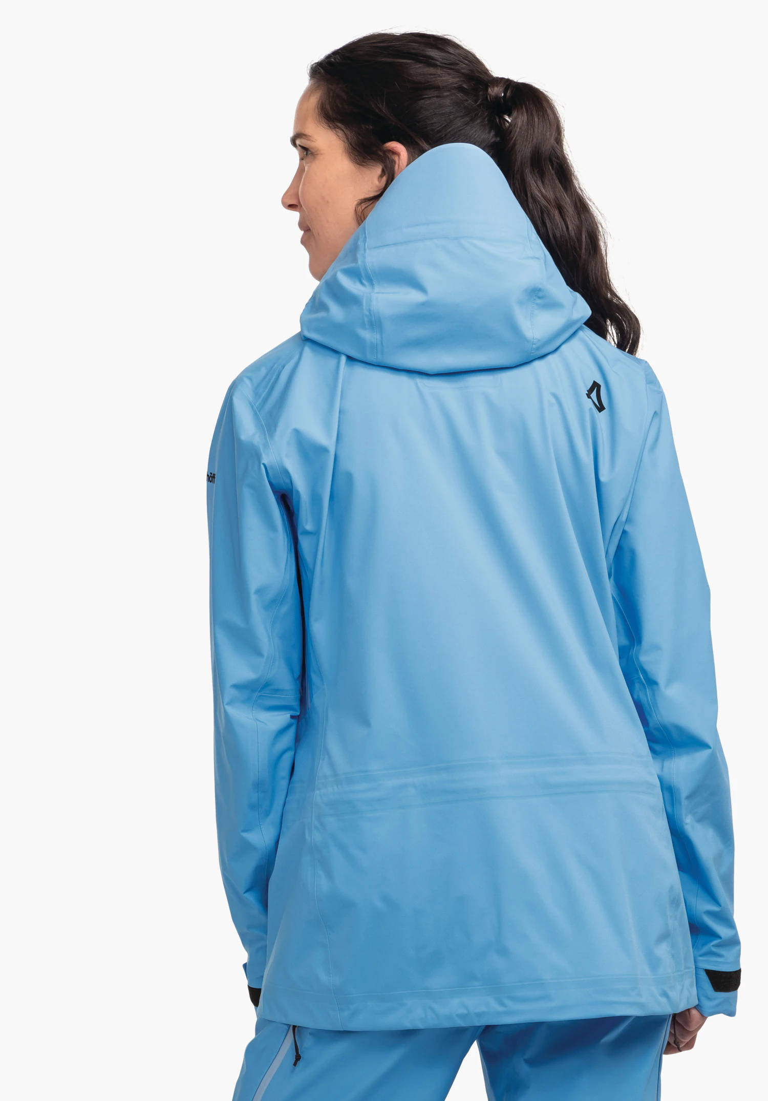 Jacket Style Milagle WMS Hellblau Regenjacke wird von einer Frau getragen, sie steht mit dem Rücken zur Kamera und schaut zur Seite; Kapuze hochgezogen, Schöffel-Logo sichtbar; weißer Studiohintergrund.