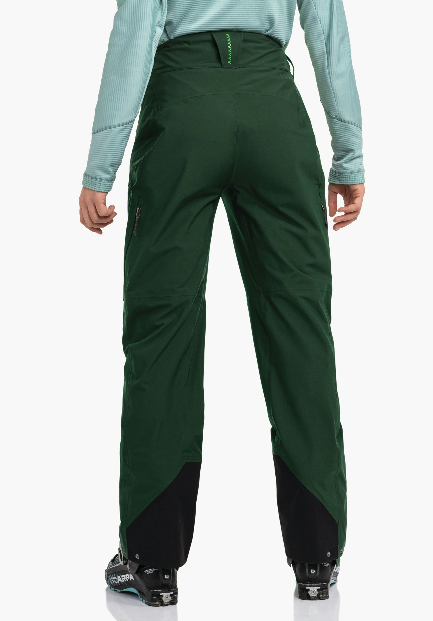 Pants Style Milagle WMS Dunkelgrüne Hose, Rückansicht, getragen von stehender Person; hellblaues Oberteil; schwarze Skischuhe mit Text "SCARPA"; weißer Hintergrund.