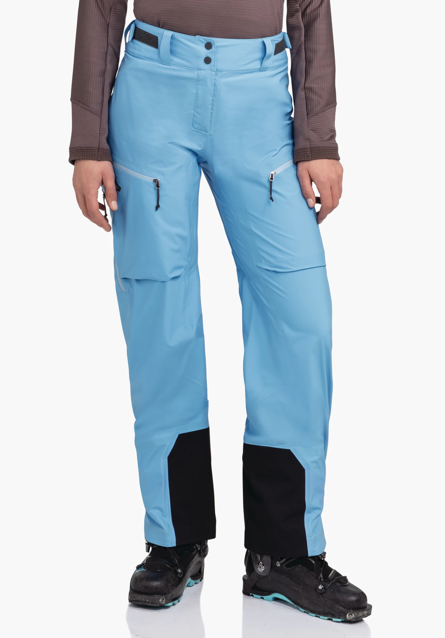 Pants Style Milagle WMS hellblaue Skihose, getragen von stehender Person, mit seitlichen Reißverschlusstaschen und schwarzen Beinverstärkungen; Person trägt schwarze Skischuhe, neutraler Hintergrund.