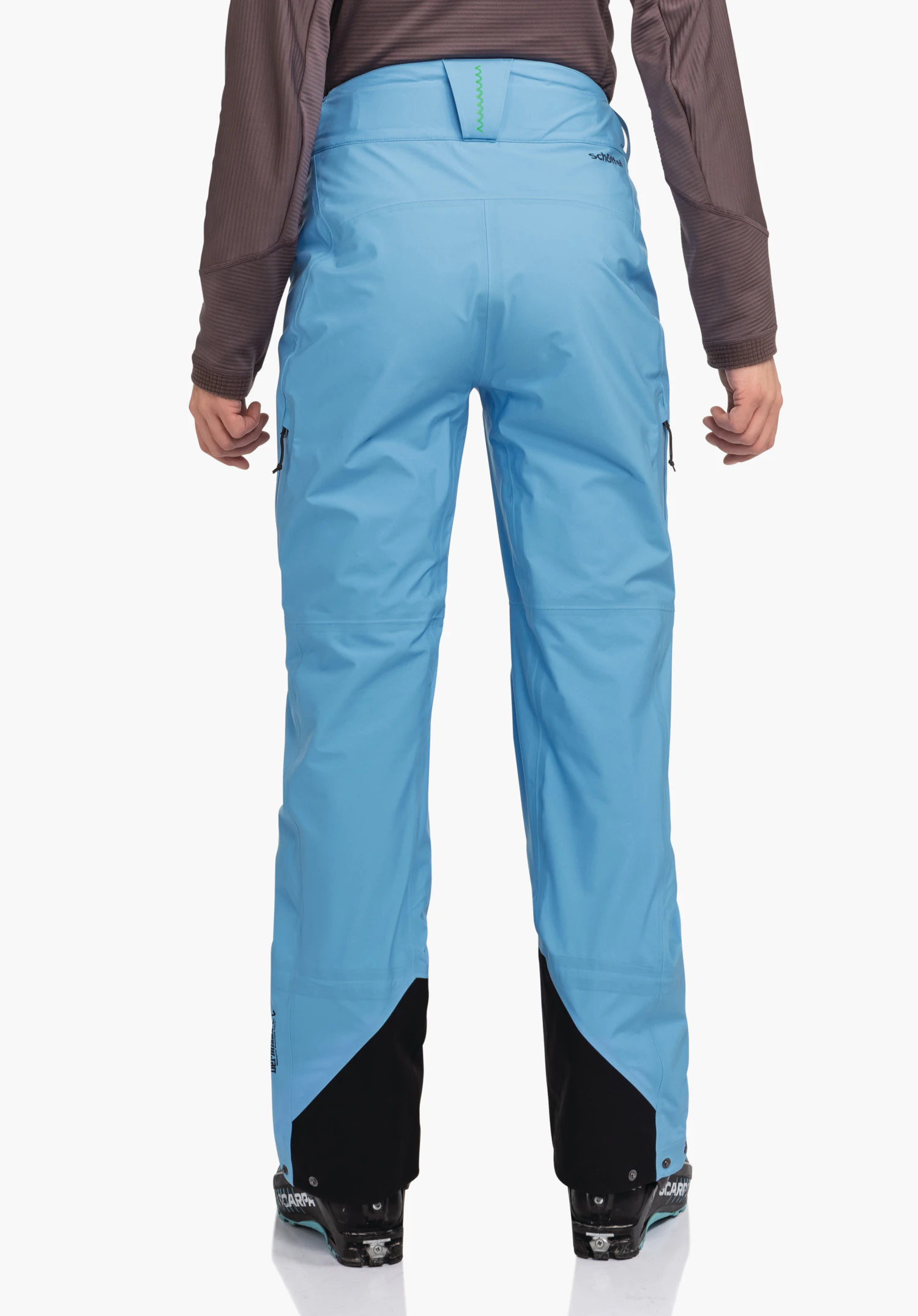 Pants Style Milagle WMS hellblaue Skihose, getragen, steht mit dem Rücken zum Betrachter; dunkelbraune Ärmel sichtbar, schwarze Skischuhe, weißer Studiohintergrund. Text: schöffel; SCARPA.