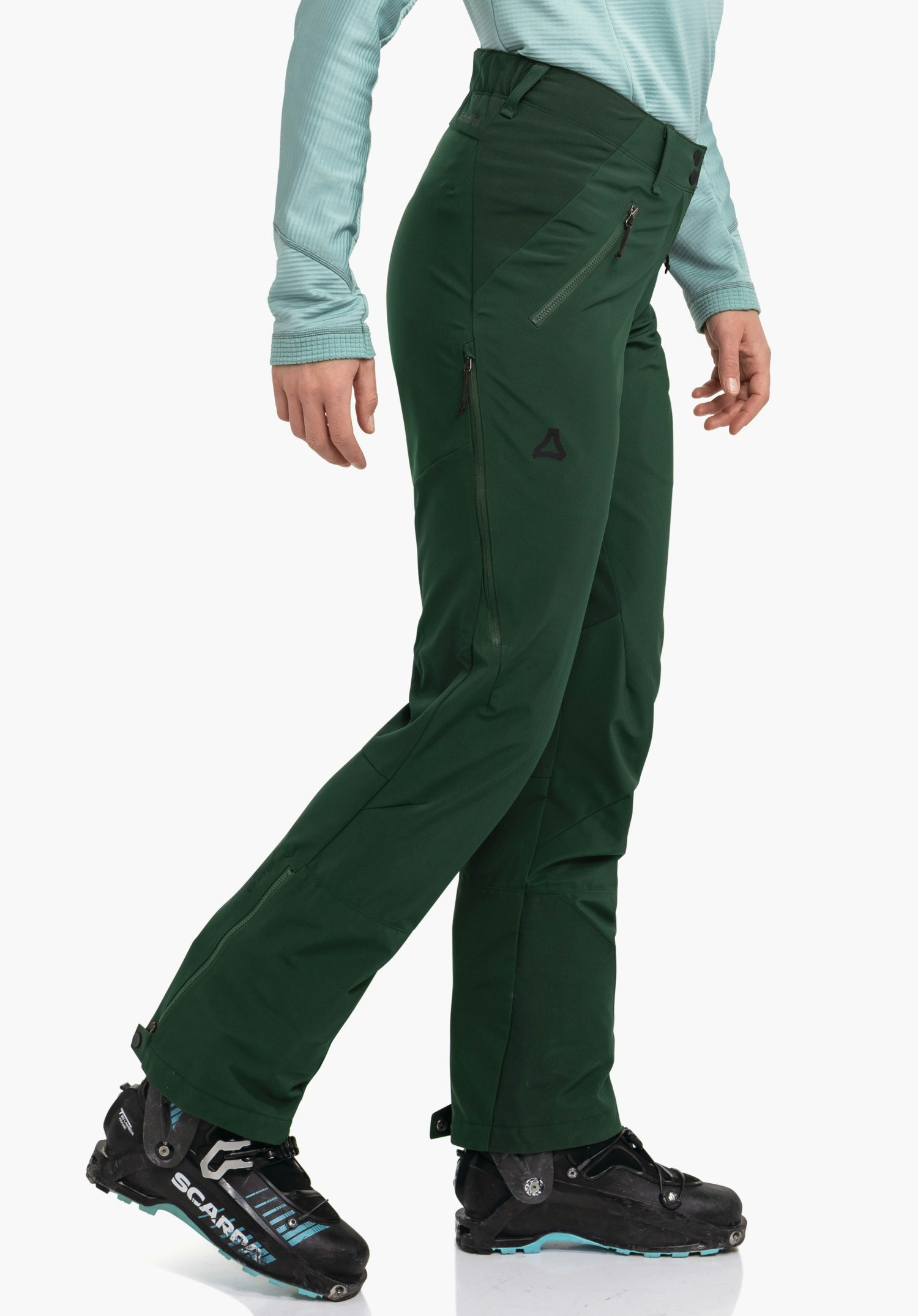 Softshell Pt Style Milagle WMS Dunkelgrüne Hose, seitlich getragen, Person dreht leicht das Bein; hellblaues Langarmshirt, schwarze Bergstiefel mit Schrift "SCARPA"; Schöffel-Logo auf Oberschenkel; weißer Hintergrund.