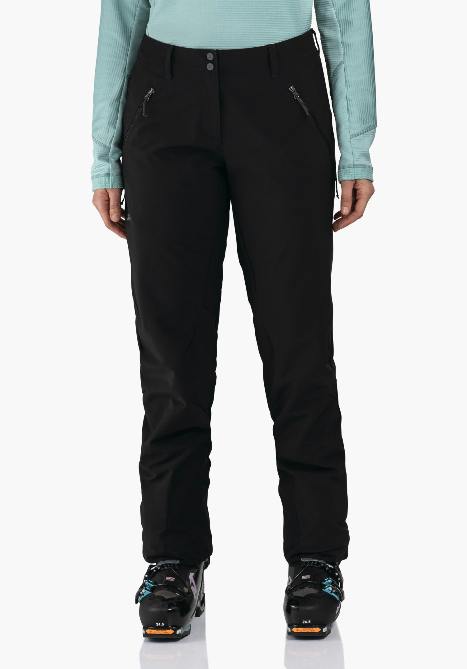 Softshell Pt Style Milagle WMS pantalon de ski noir porté par une personne debout, avec poches zippées diagonales; contexte:haut manches longues bleu clair, chaussures de ski noires. Texte sur les chaussures:"24.5". Logo Schöffel sur la hanche gauche.