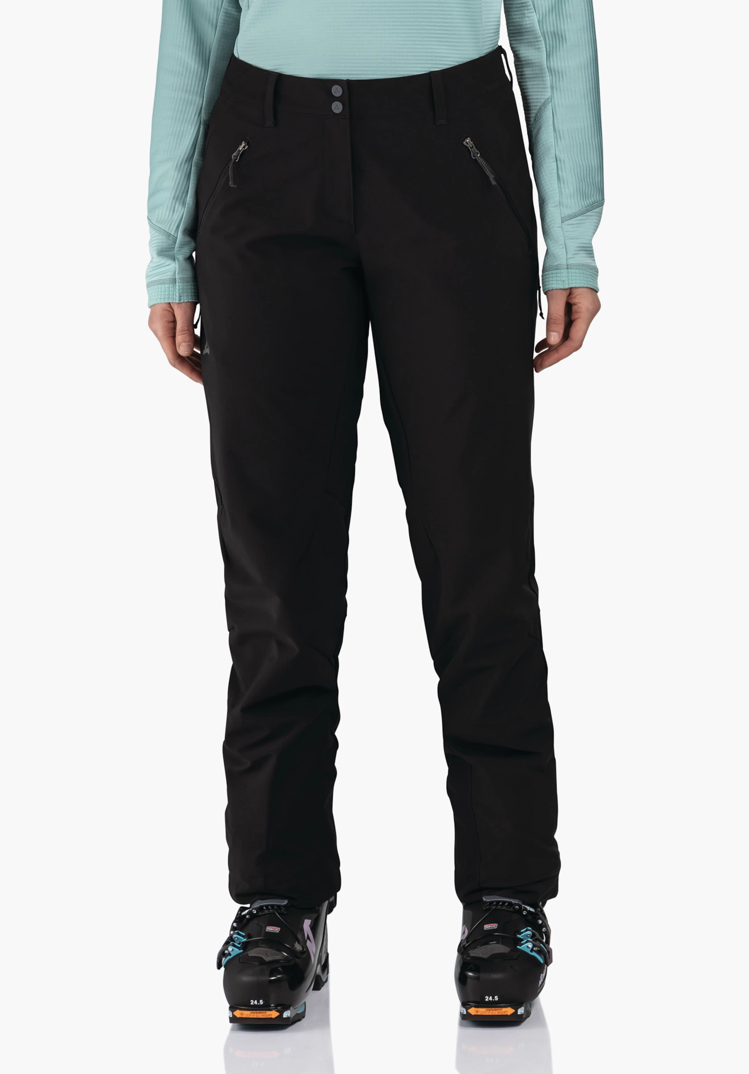 Softshell Pt Style Milagle WMS pantalon de ski noir porté par une personne debout, avec poches zippées diagonales; contexte:haut manches longues bleu clair, chaussures de ski noires. Texte sur les chaussures:"24.5". Logo Schöffel sur la hanche gauche.