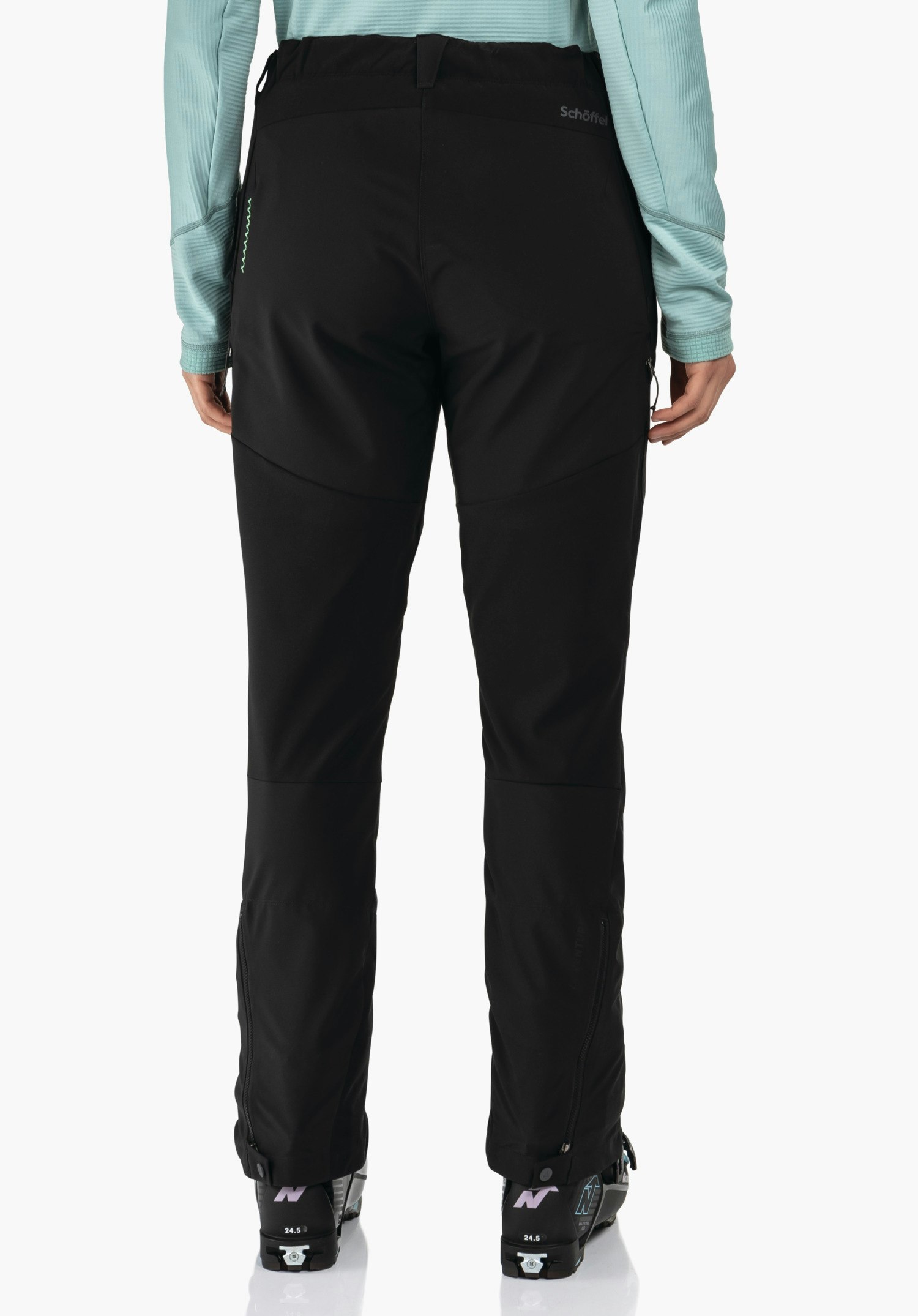 Softshell Pt Style Milagle WMS pantalon outdoor noir, porté de dos; personne portant un haut manches longues turquoise clair et des chaussures de ski noires; bas de jambes zippés. Texte: « Schöffel », sur les chaussures « N », « 24.5 ».