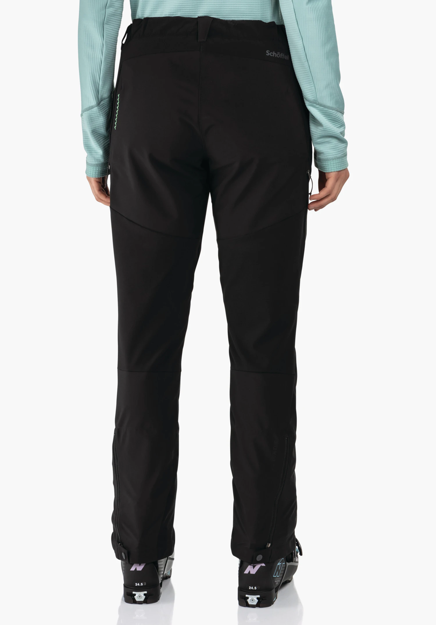 Softshell Pt Style Milagle WMS pantalon outdoor noir, porté de dos; personne portant un haut manches longues turquoise clair et des chaussures de ski noires; bas de jambes zippés. Texte: « Schöffel », sur les chaussures « N », « 24.5 ».