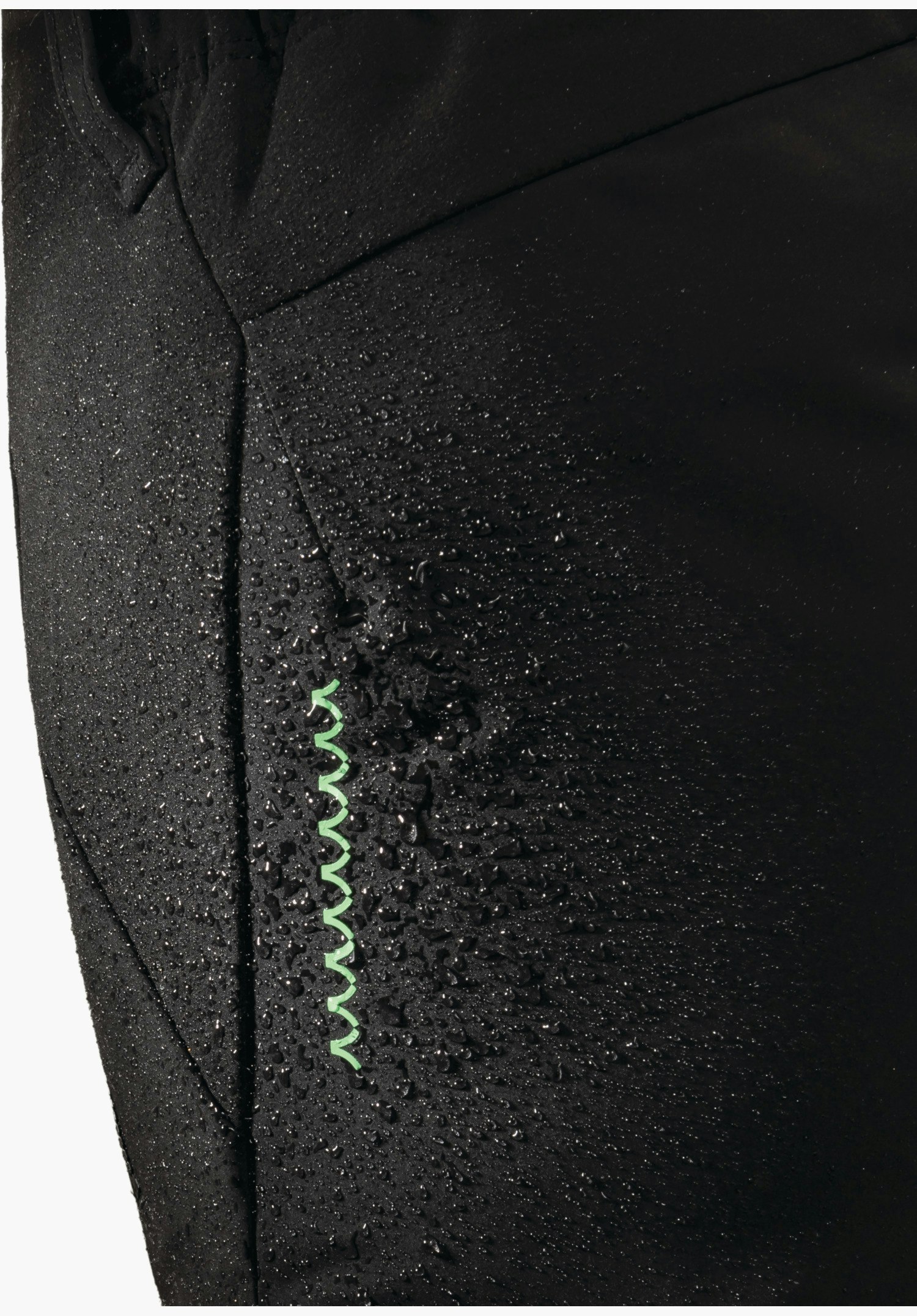Softshell Pt Style Milagle WMS montre la surface déperlante du tissu noir avec des gouttelettes d'eau et un élément de design en zigzag vert en gros plan sur un fond blanc/neutre.