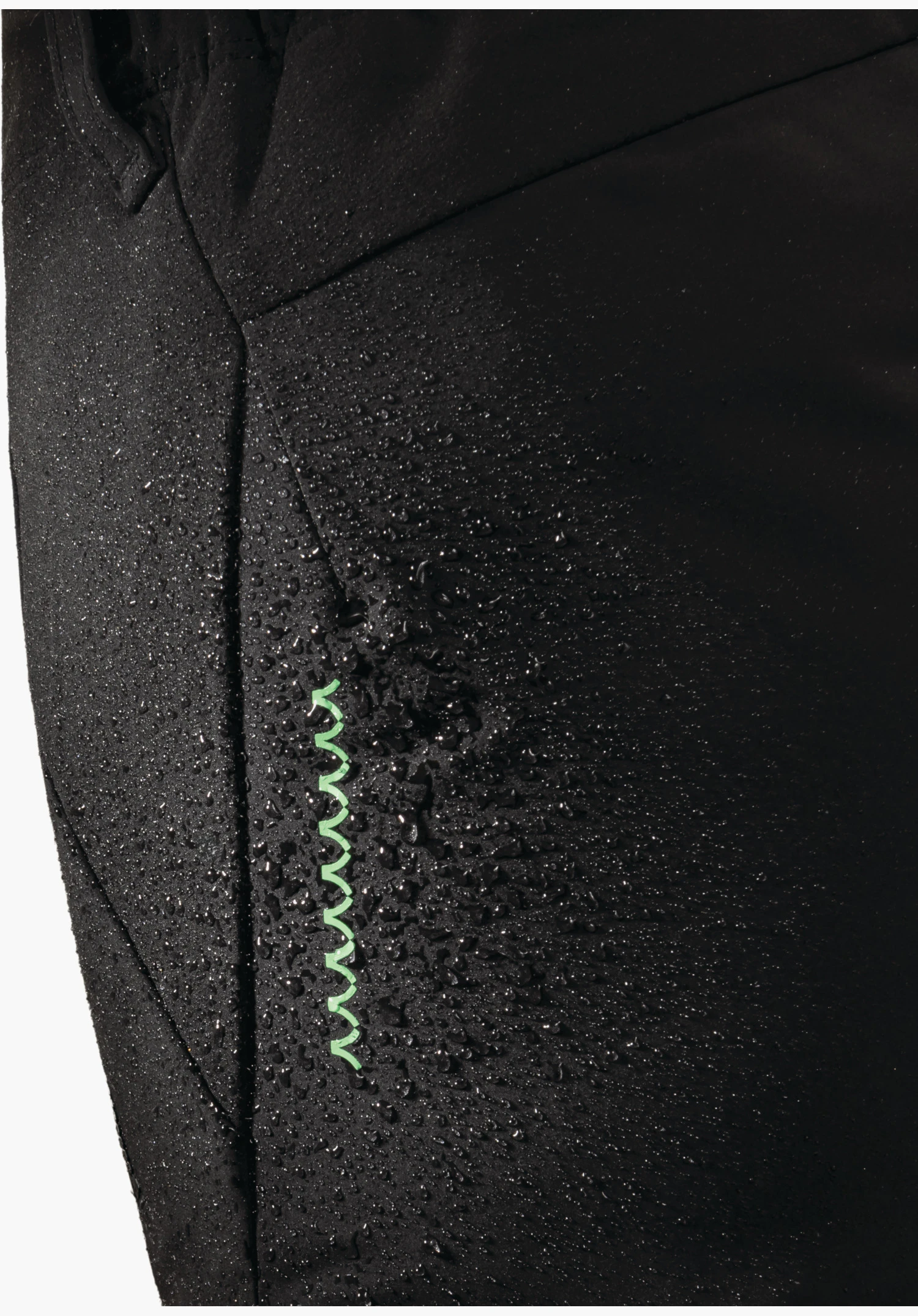 Softshell Pt Style Milagle WMS montre la surface déperlante du tissu noir avec des gouttelettes d'eau et un élément de design en zigzag vert en gros plan sur un fond blanc/neutre.