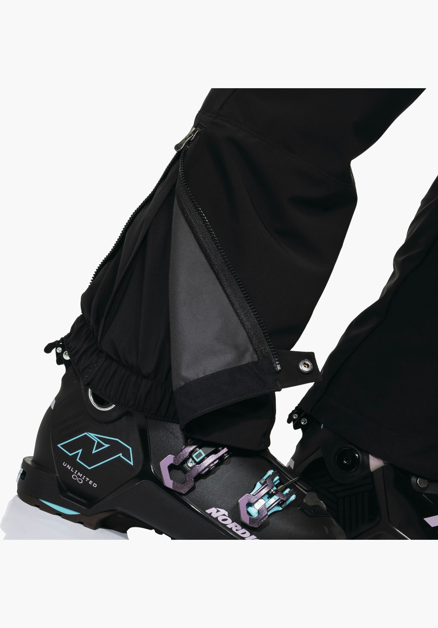 Softshell Pt Style Milagle WMS montrant le bas de jambe noir avec zip ouvert et soufflet d'aisance pour le réglage de la largeur ainsi que la guêtre pare-neige intégrée au-dessus de la chaussure de ski. Gros plan sur fond blanc/neutre.