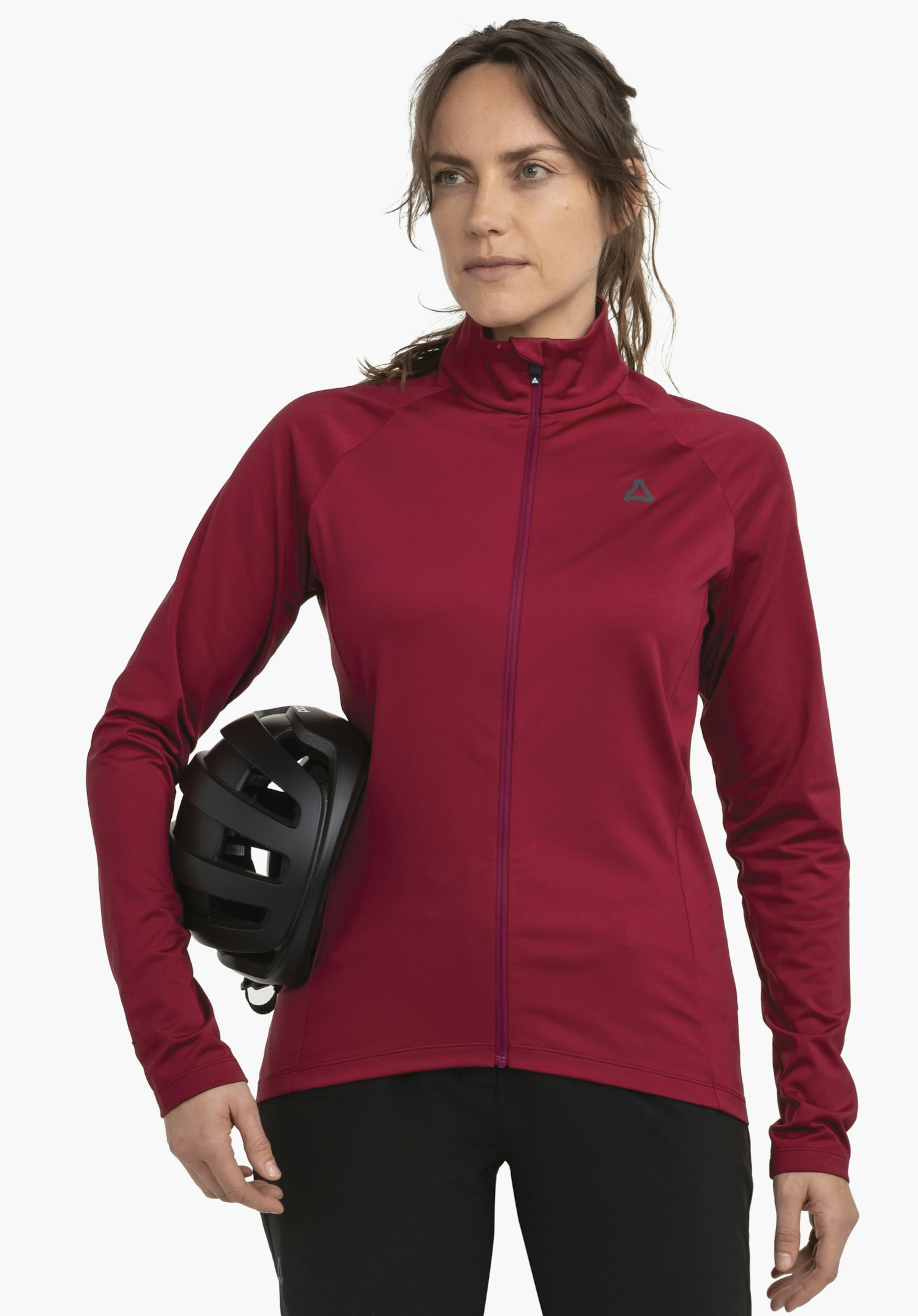 Longsleeve Style Kubena WMS Frau trägt dunkelrote Jacke, hält einen schwarzen Fahrradhelm an der Hüfte; Schöffel-Logo auf der Brust; trägt schwarze Hosen; steht vor hellem Hintergrund.