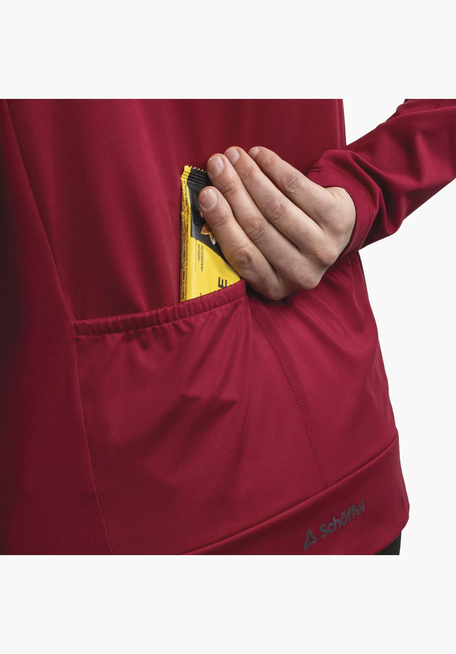 Longsleeve Style Kubena WMS, détail de la poche arrière rouge utilisée et du logo Schöffel sur l'ourlet, gros plan sur fond neutre.
