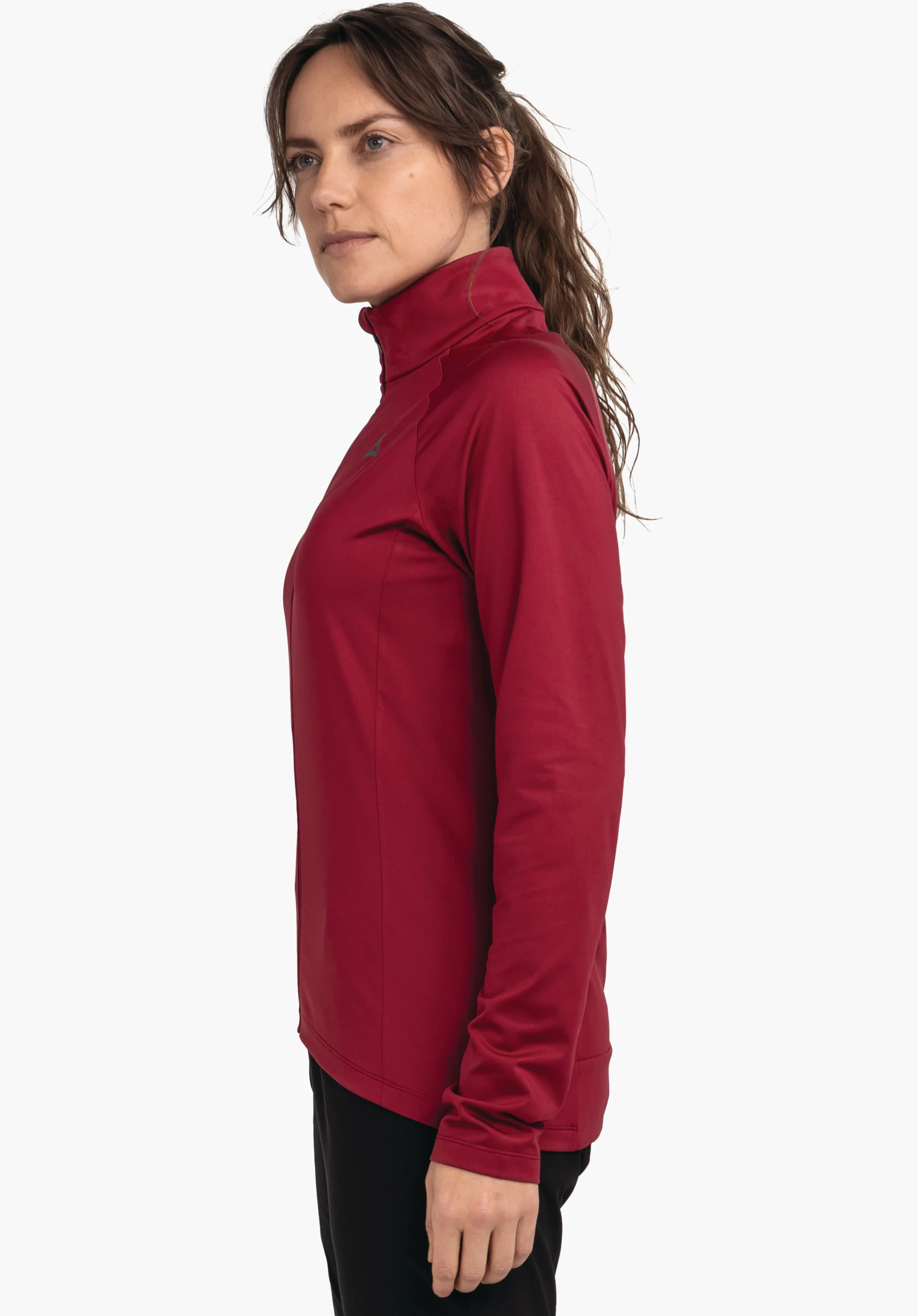 Longsleeve Style Kubena WMS veste de sport rouge foncé à col montant; femme la porte debout de profil, regard vers l’avant; logo Schöffel sur la poitrine; tissu lisse, pantalon noir, fond blanc.