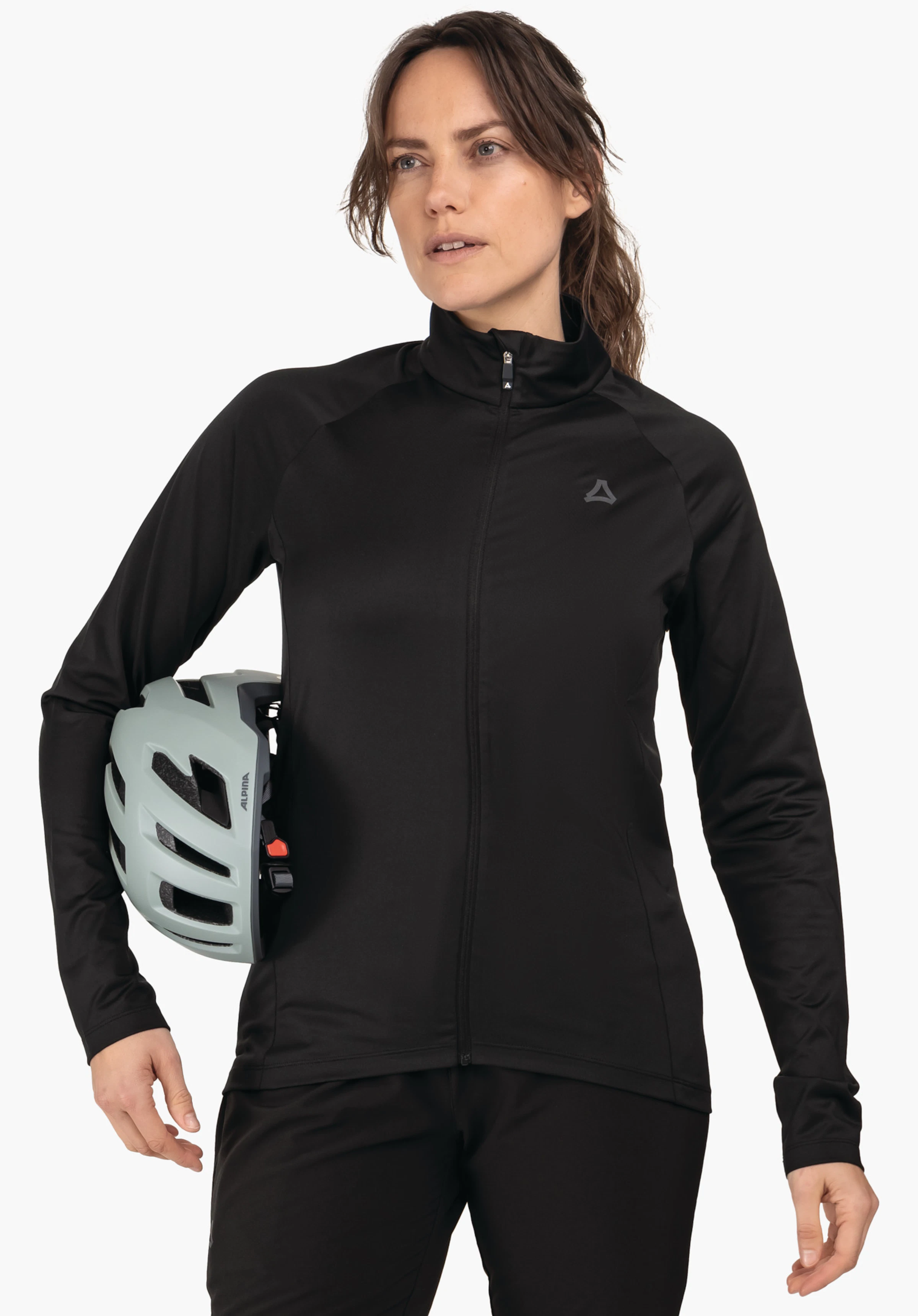 Longsleeve Style Kubena WMS zwarte jas met Schöffel-logo, gedragen door een vrouw die een lichtgroene fietshelm onder de arm houdt (opschrift: ALPINA); staande pose voor een witte achtergrond.