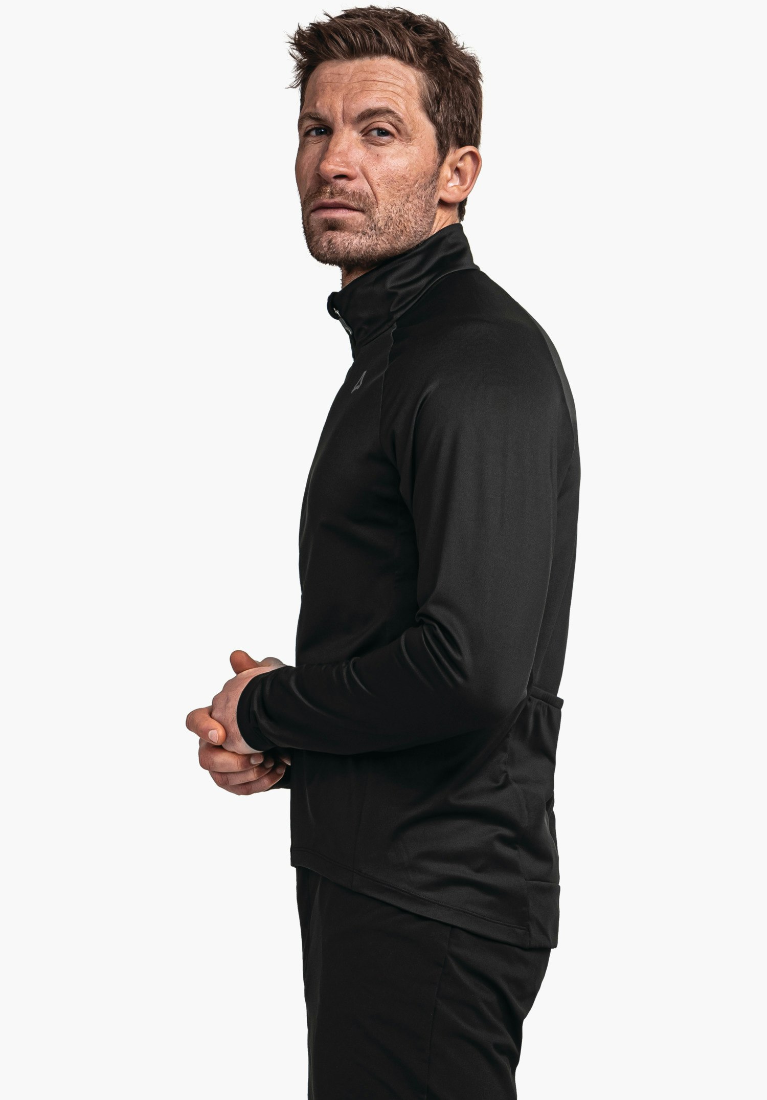 Longsleeve Style Kubena MNS Schwarze Trainingsjacke, Mann steht seitlich mit gefalteten Händen, Schöffel-Logo sichtbar auf der Brust, neutraler weißer Hintergrund.