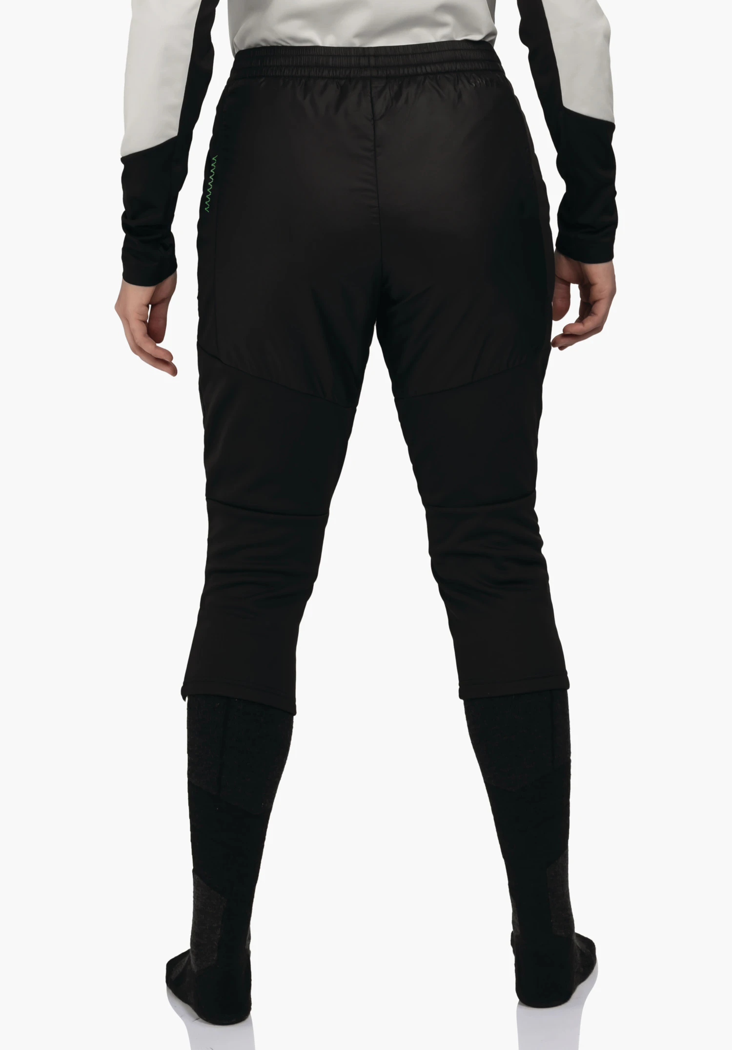 3/4 Pants Style Lufillo WMS zwarte trekkingbroek, van achteren gedragen; persoon staat met ontspannen hangende handen, lichtwitte mouwen met zwarte inzetten, donkergrijze en zwarte kniekousen, witte achtergrond.
