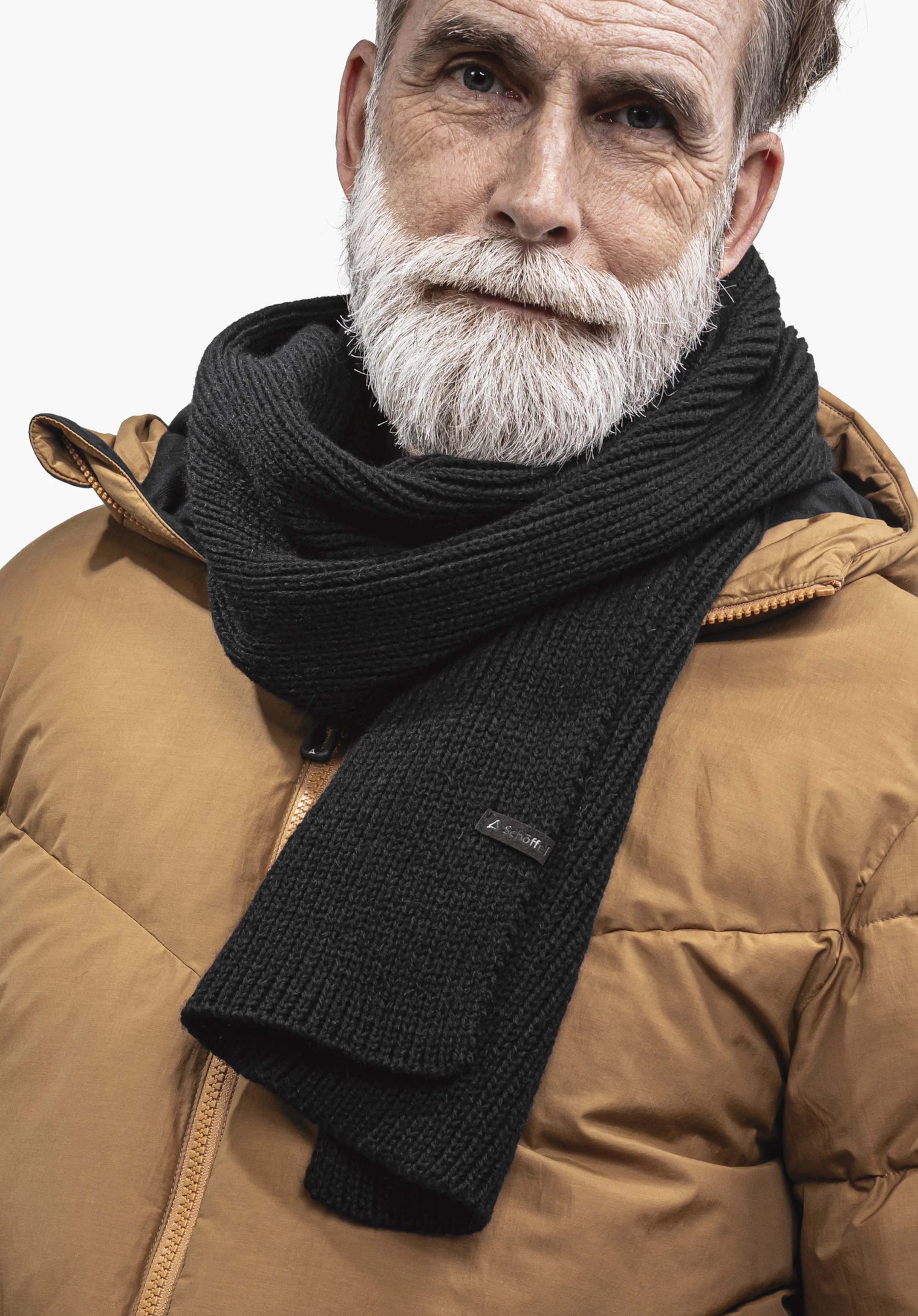 Scarf Style Boslix ALL Écharpe noire enroulée autour de la barbe blanche d’un homme âgé, portée sur une doudoune marron clair; petite étiquette avec logo Schöffel sur l’écharpe, fond blanc.