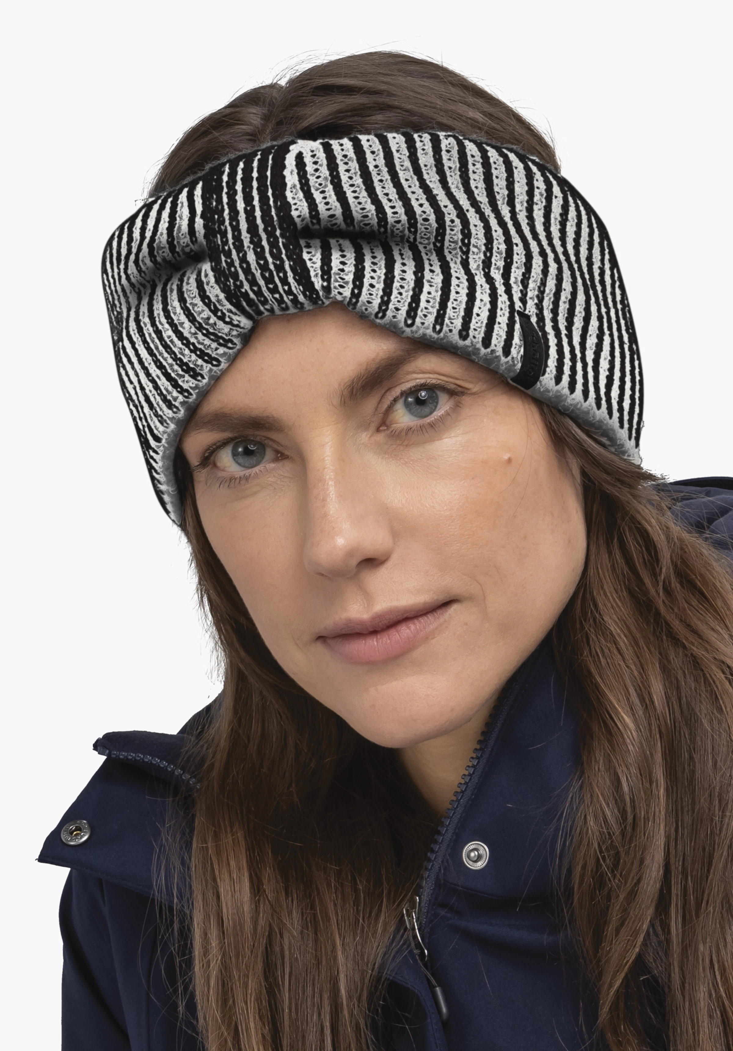 Headband Style Cledio ALL Knitted headband, black and off-white striped, sits twisted over the forehead; worn by a woman with a dark blue jacket, visible face, neutral light background.