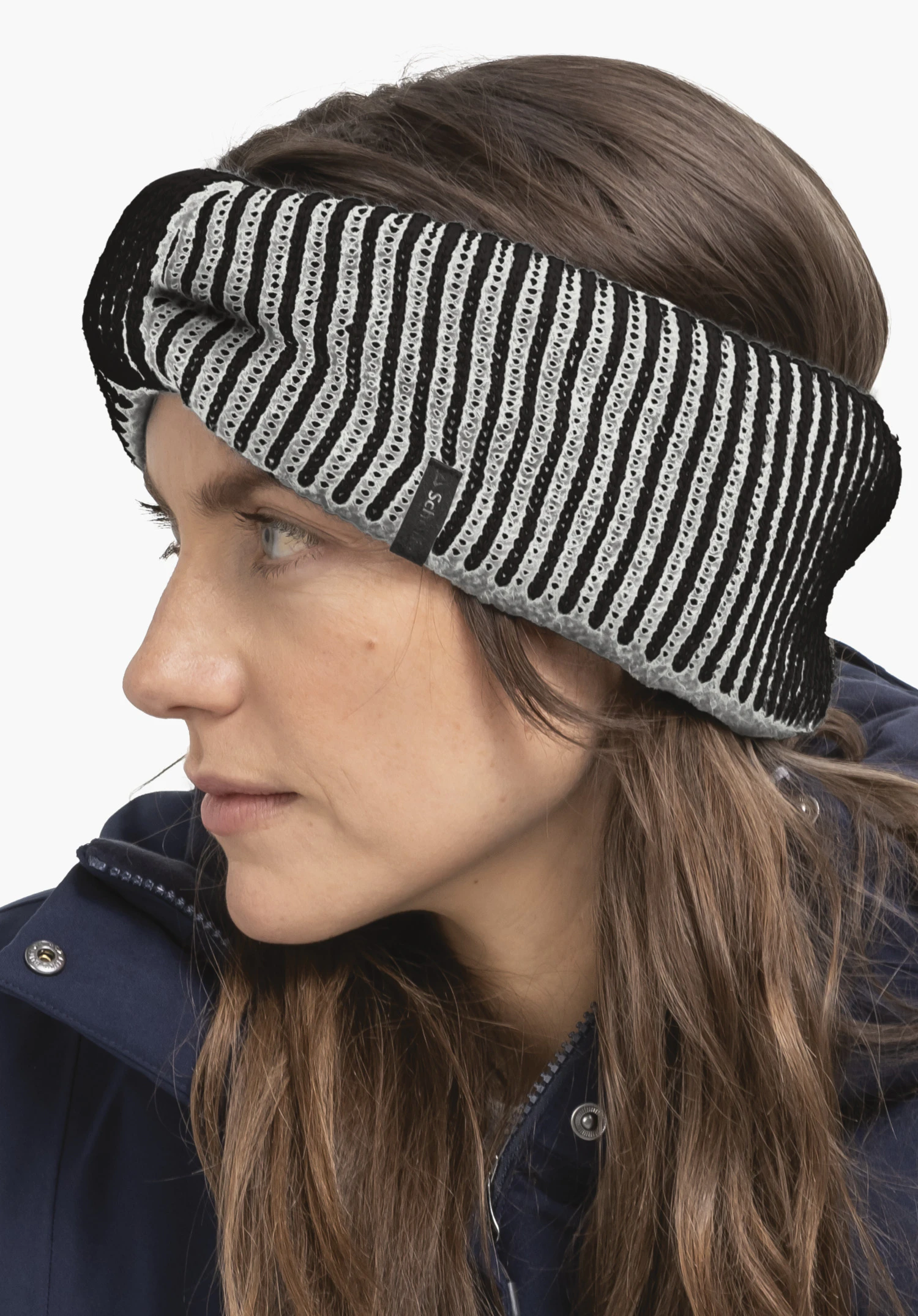 Headband Style Cledio ALL white and black striped headband, crossed at the front, worn snugly on a woman’s head; side portrait; she wears a dark blue coat; light neutral background.