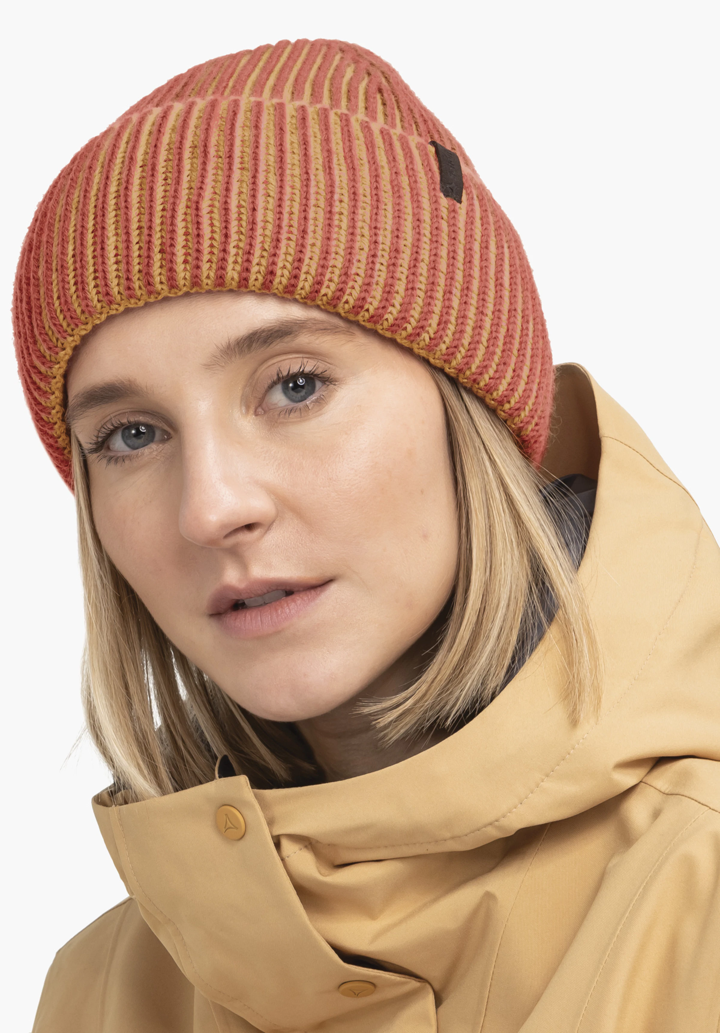 Hat Style Wildkar ALL Pink knitted beanie with Schöffel logo worn by a blonde woman; she wears a yellow jacket; light plain background.