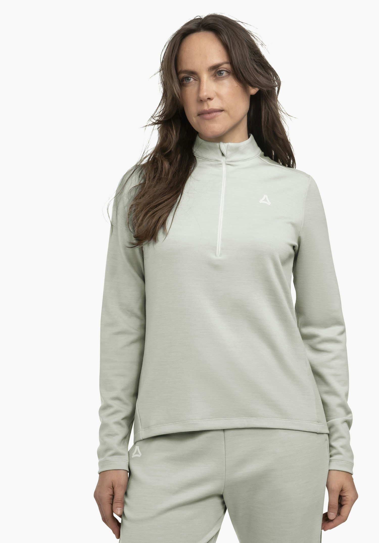 Longsleeve Style Canyfer WMS Haut manches longues bleu clair avec zip court; femme le porte et se tient légèrement de côté; pantalon bleu clair assorti; fond clair neutre; logo Schöffel visible sur la poitrine et le pantalon.