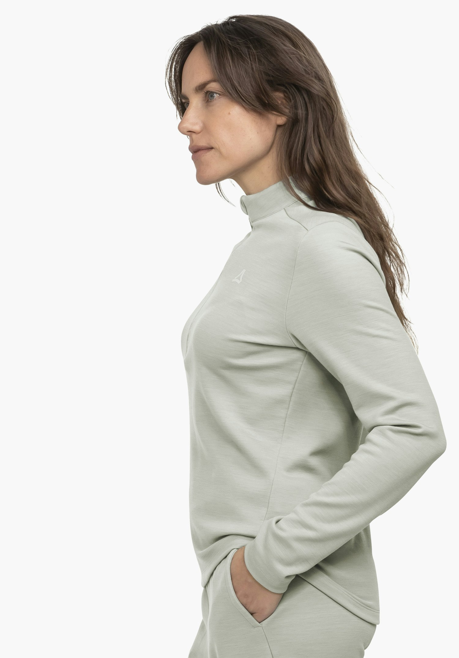Longsleeve Style Canyfer WMS Frau steht seitlich; sie trägt ein hellblaues Langarmshirt mit Schöffel-Logo, eine Hand in Hosentasche, schlichter weißer Hintergrund.