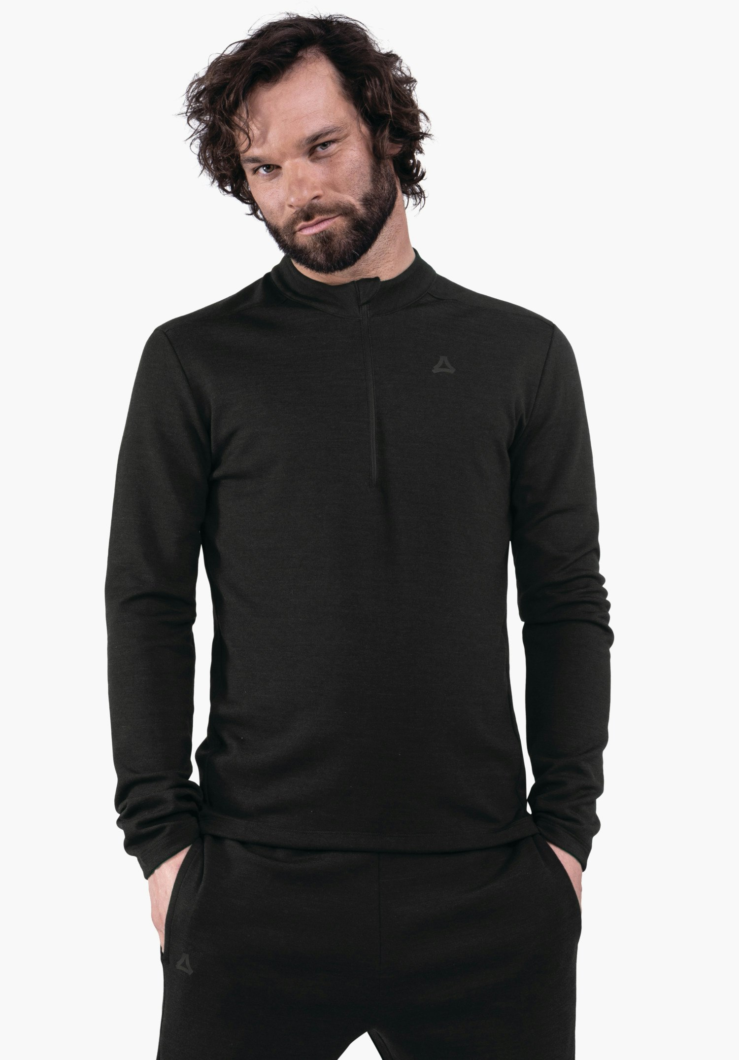 Longsleeve Style Canyfer MNS Mann trägt einen dunkel schwarzen Pullover mit halbem Reißverschluss, Hände in Hosentaschen, steht vor weißem Hintergrund; Schöffel-Logo auf Brust und Hose.